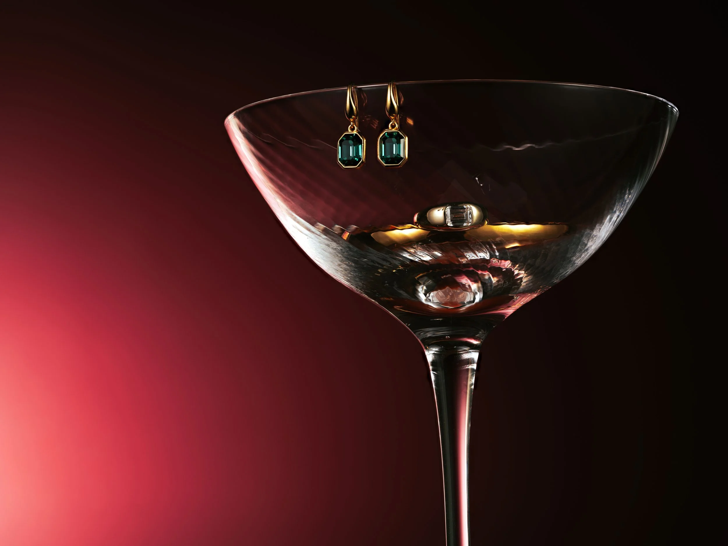 A pair of turquoise gemstone earrings hanging inside a crystal cocktail glass with a dark background.
