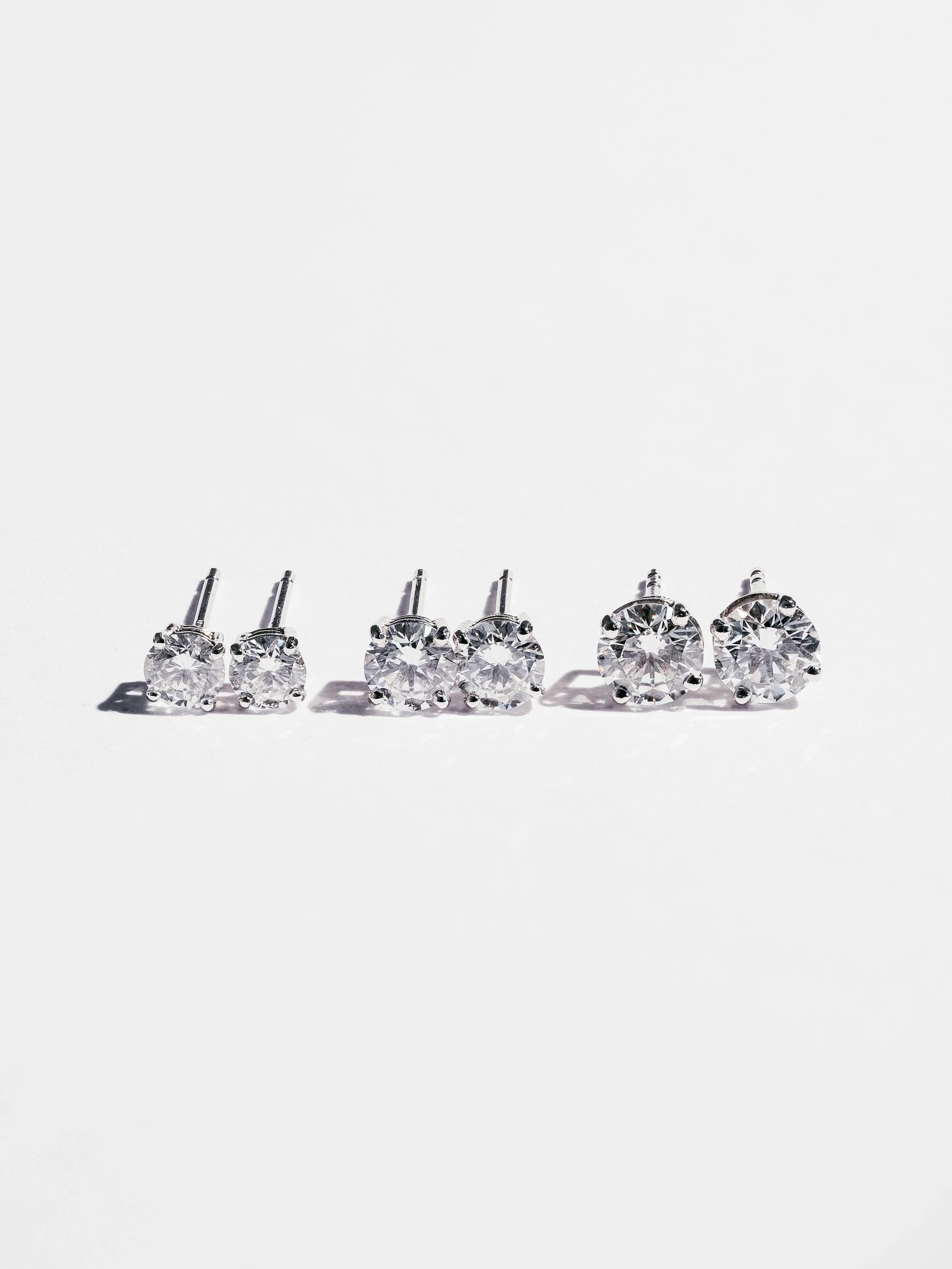 Three pairs of diamond stud earrings arranged in increasing size from left to right on a white background.