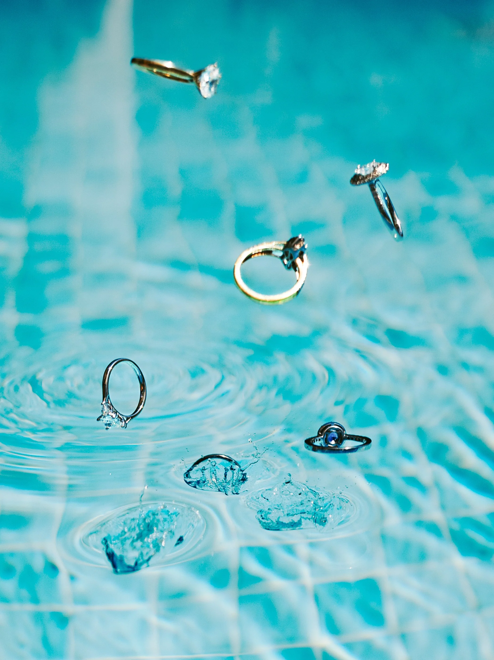 Jewelry pieces, including rings and earrings, falling into a swimming pool with water ripples.