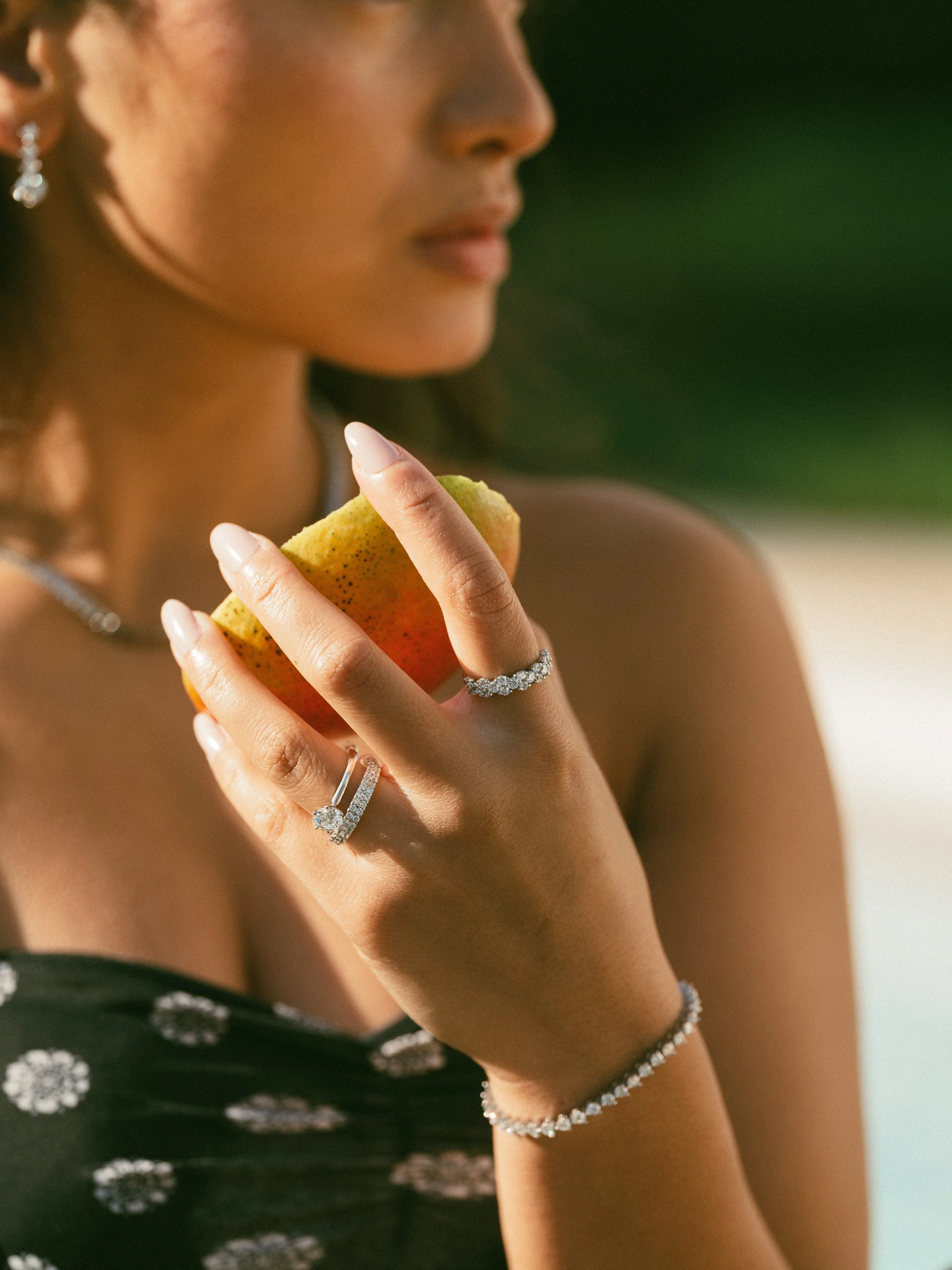 Woman holding a pear, wearing jewelry, with blurred green background.