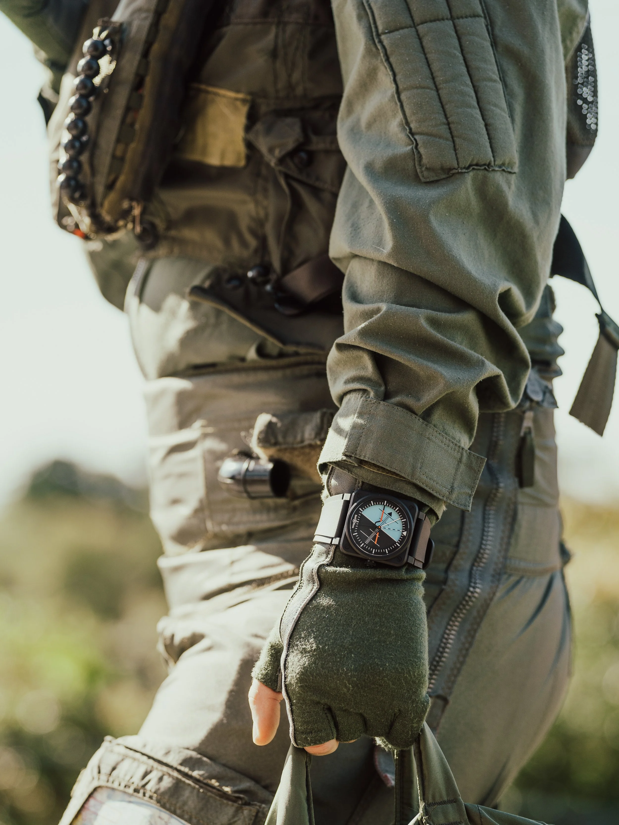 Close-up of a person dressed in tactical military gear, wearing a watch on their left wrist, outdoors.