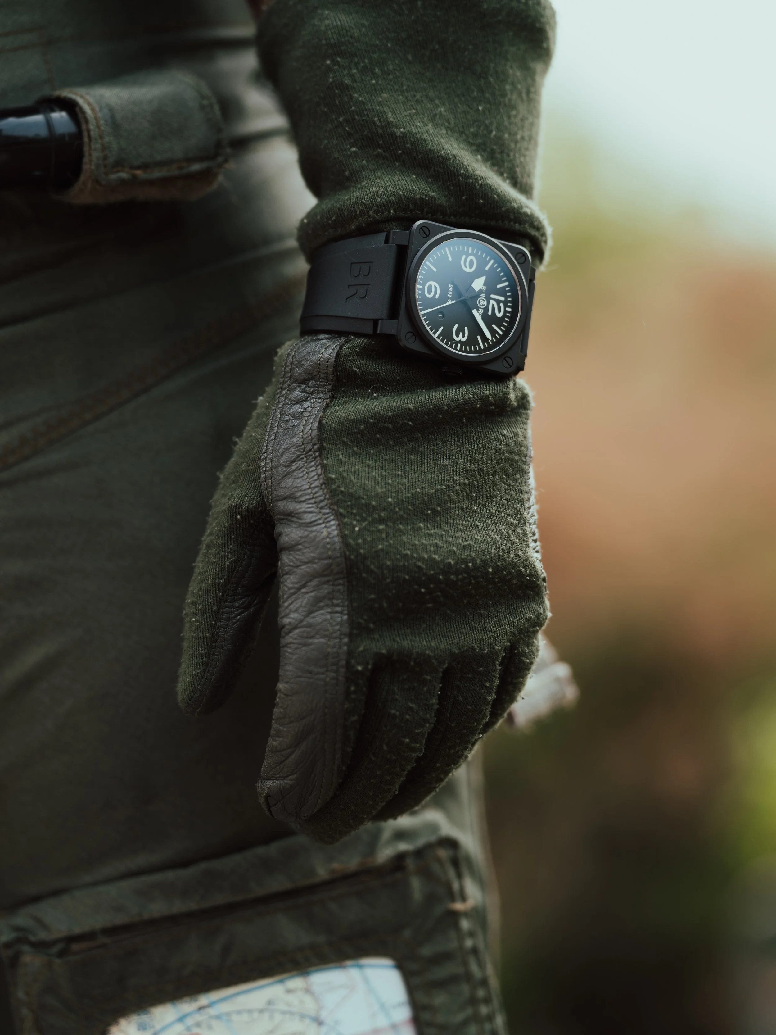 A person wearing a green long-sleeve shirt, gray gloves, and a black wristwatch with a black strap.