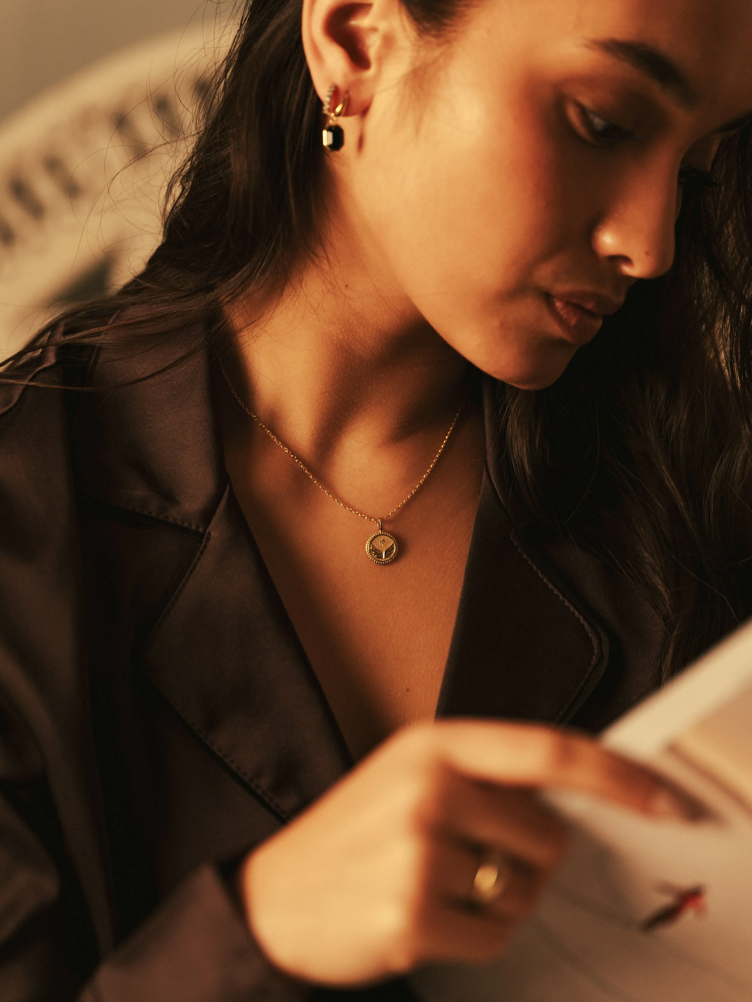 Close-up of a woman with dark hair, wearing earrings and a necklace, reading a book.