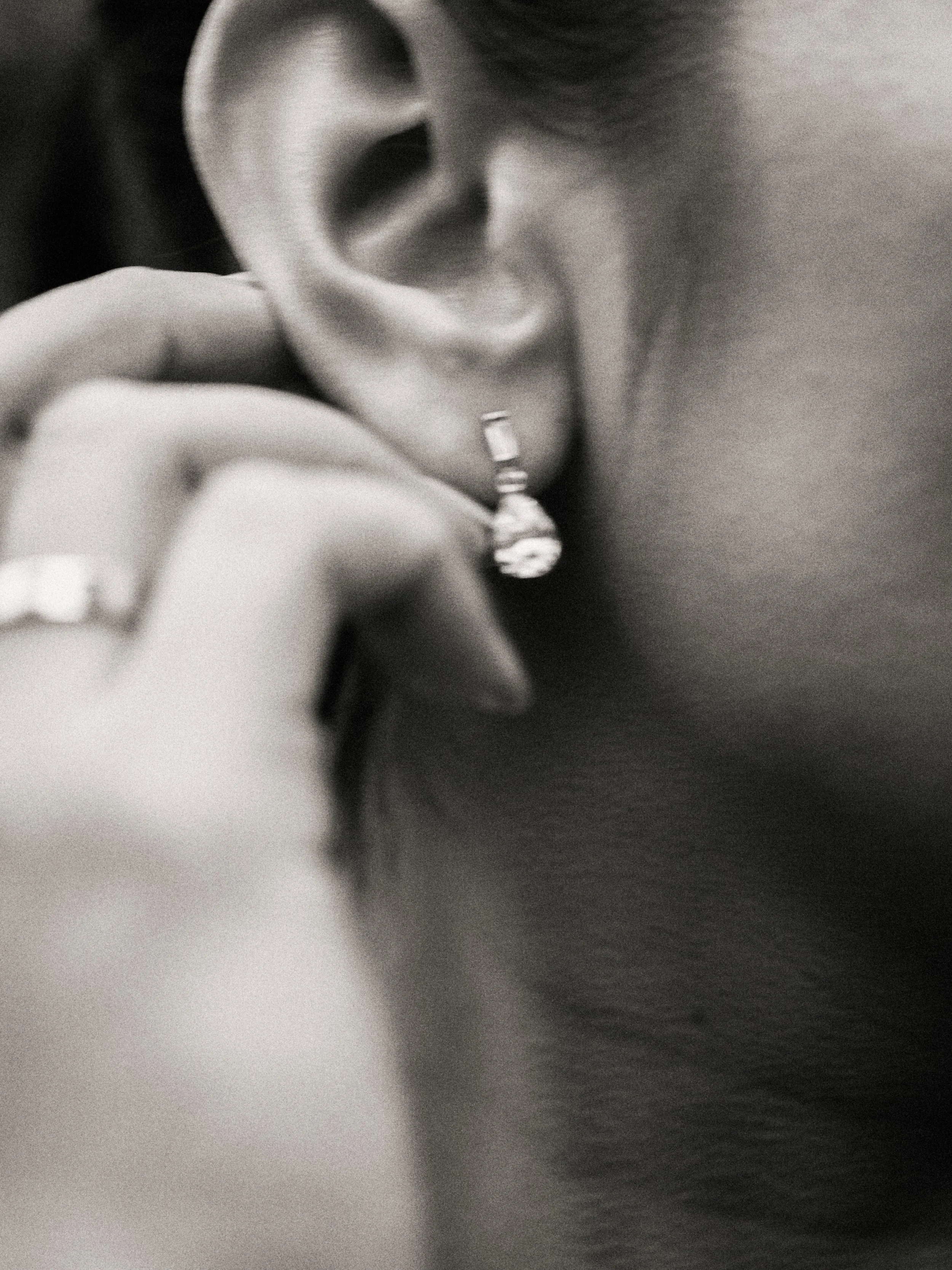 Close-up of a person's ear with a dangling earring, and a hand with a ring touching the ear.