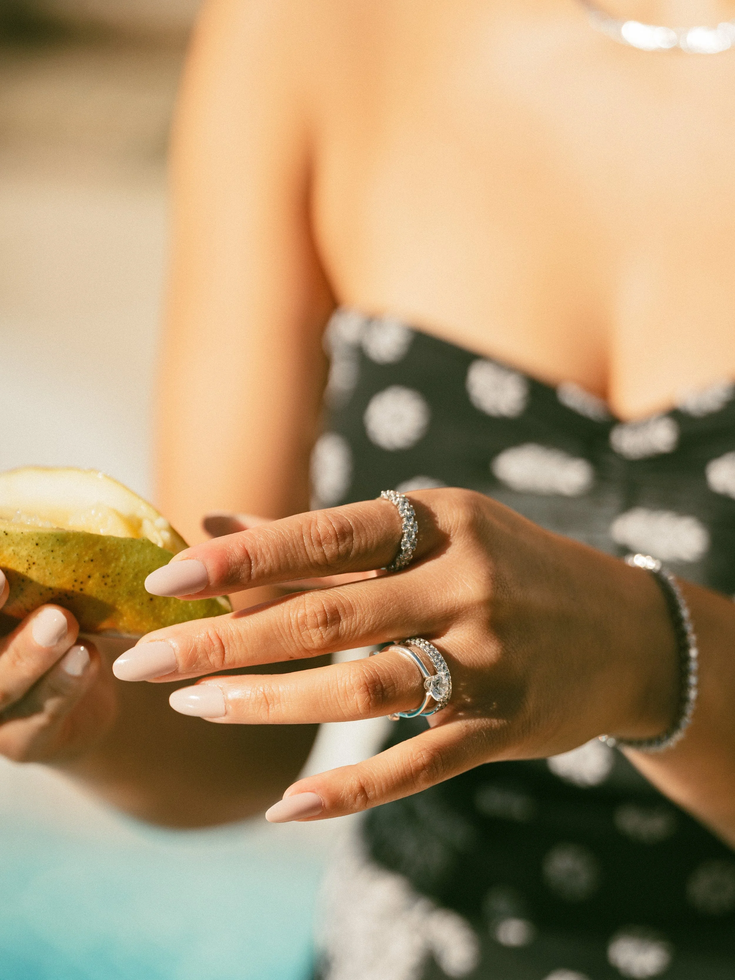 Close-up of a woman’s hand with jewelry, holding a pear and a slice of pear, dressed in a black dress with white polka dots.