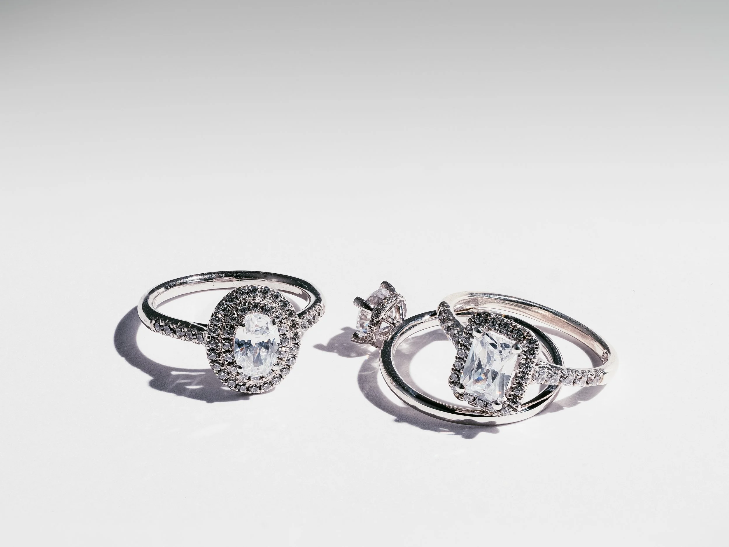 Three silver rings with large gemstones and smaller stones on a white background, casting shadows.