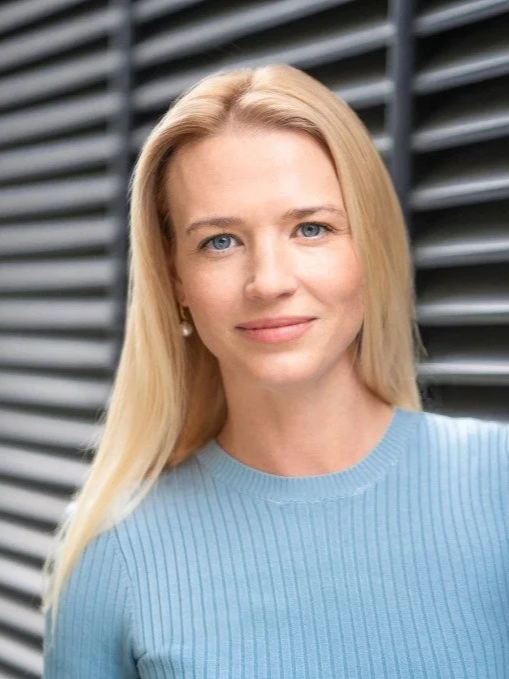 Close-up of woman with blonde hair, light skin, blue jumper, in an indoor setting with warm lighting