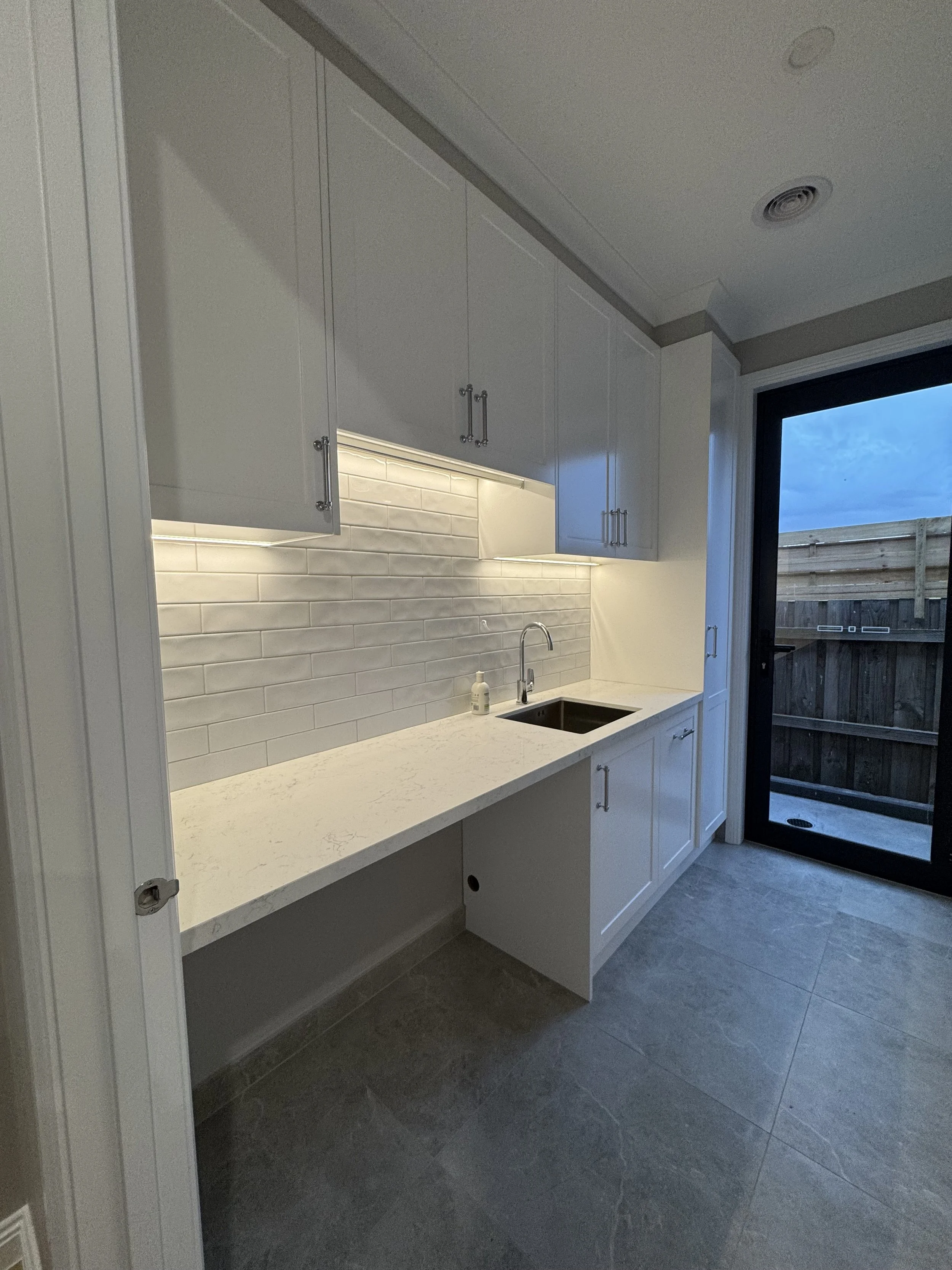 Modern kitchen with white cabinets, a white granite countertop, a black undermount sink, and a sliding glass door leading outside.