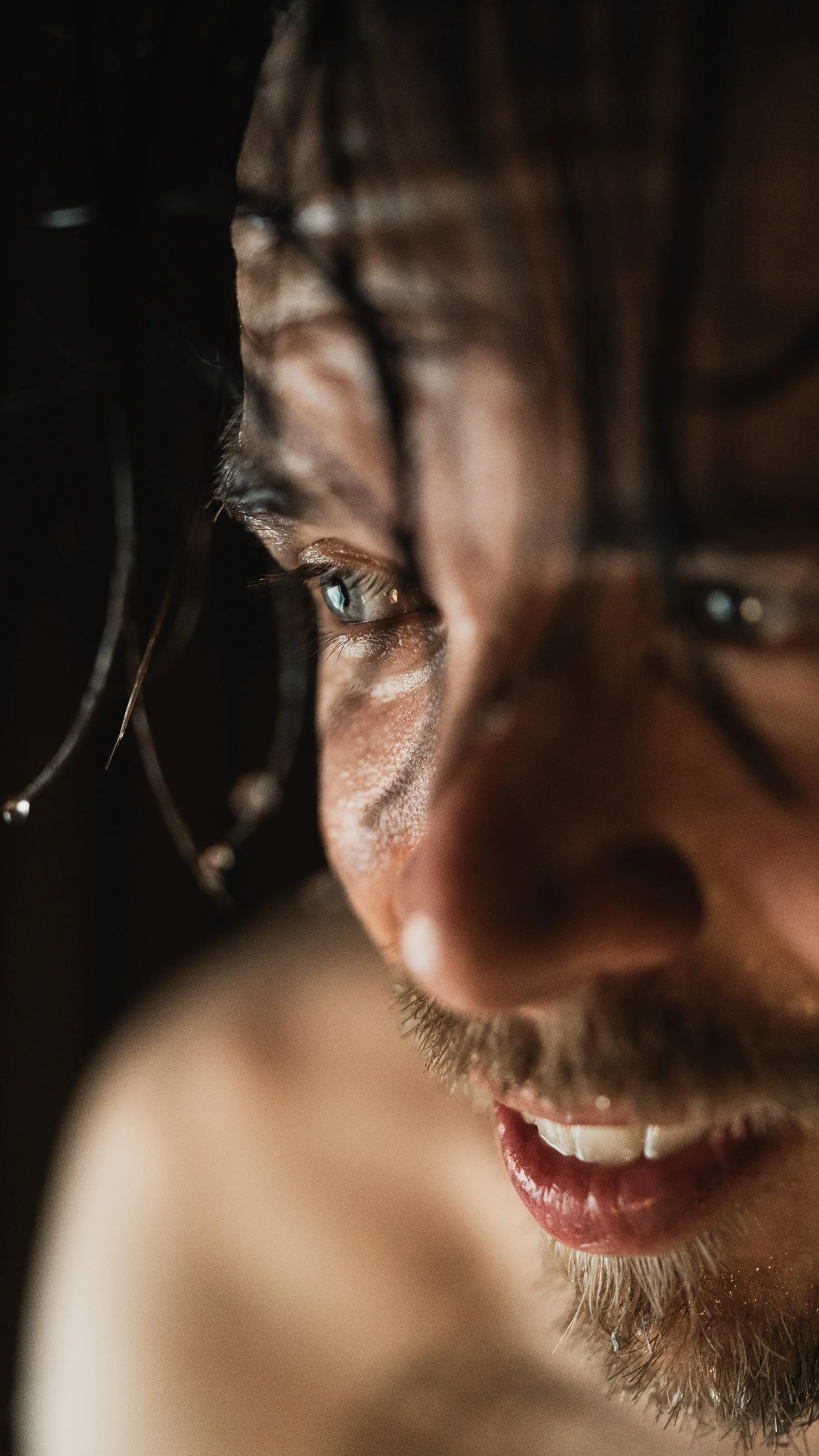 Sauna in Rovaniemi. Close-up of a person's face with black hair, brown skin, and a goatee, smiling and looking to the side.