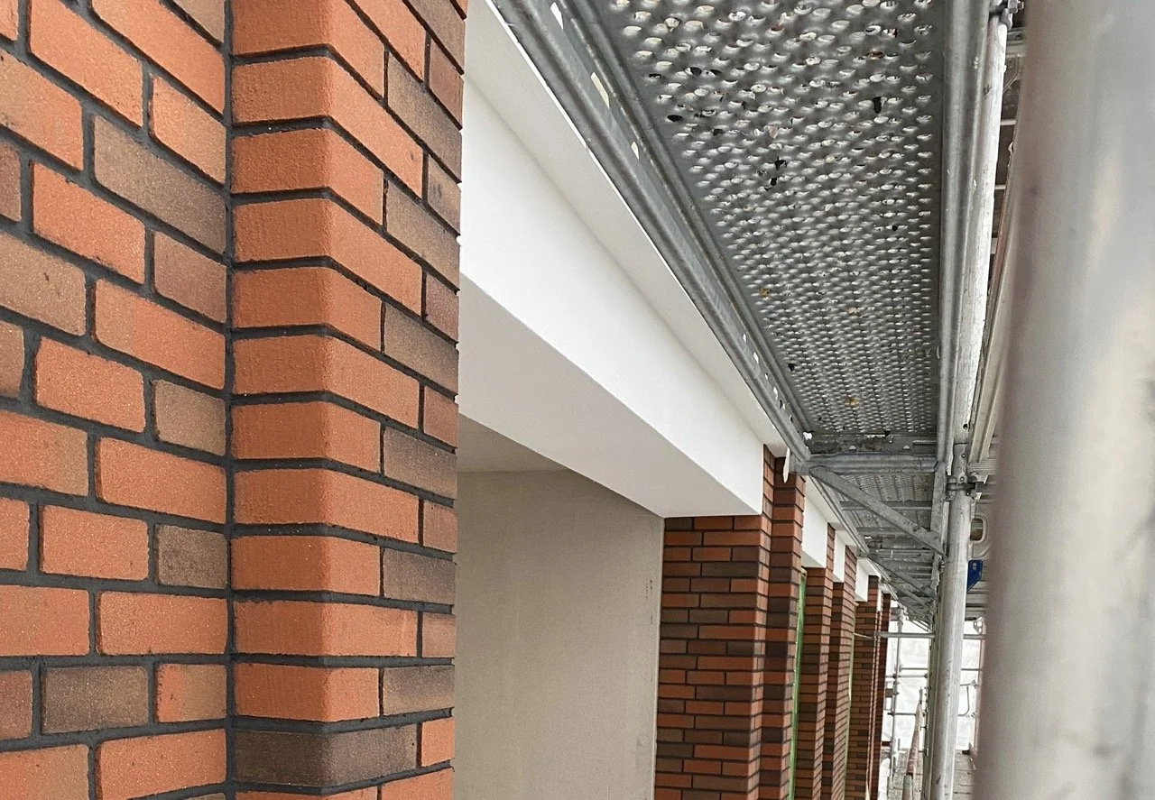 Landschap met groene heuvels, een modern gebouw, en besneeuwde bergtoppen onder een bewolkte lucht.