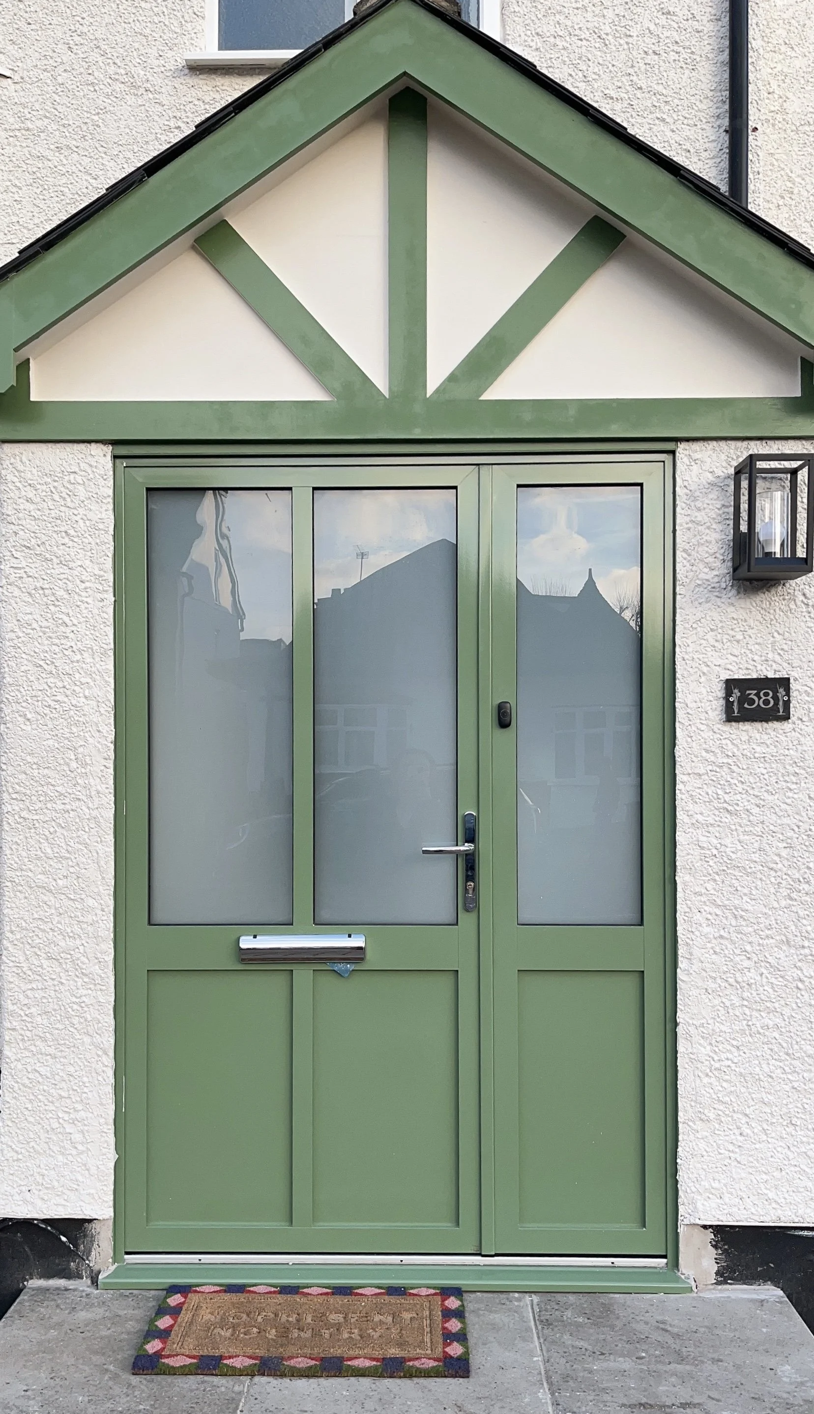 Green front door with frosted glass panes, a weatherdoormat, house number 38 on a plaque, and a black exterior wall-mounted light fixture.상징적인 연두색 대문, 영국적이고 모던한 디자인, 런던, 한인민박, 하나스테이