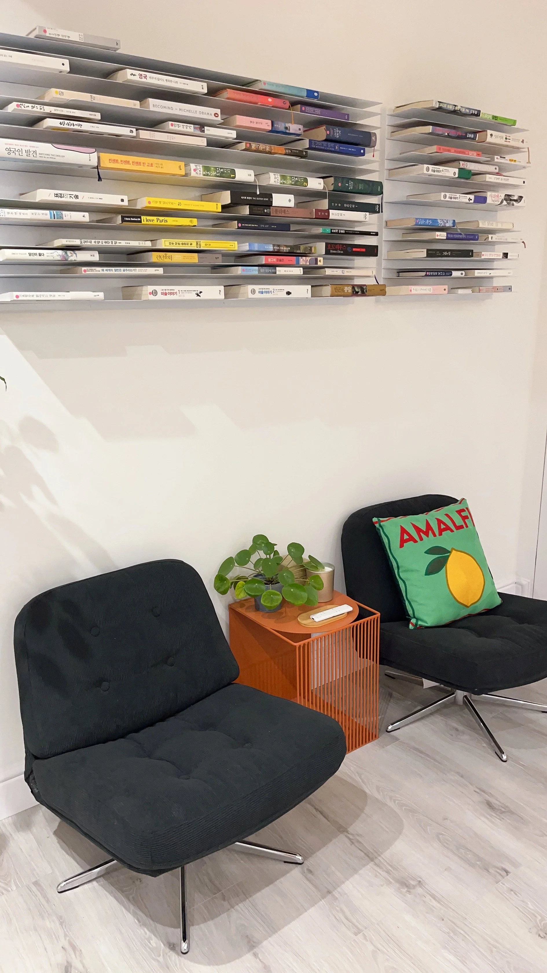 Two black armchairs with button-tufted cushions and chrome bases, a small orange side table with a green potted plant , 런던, 한인민박, 감각적 인테리어 책장