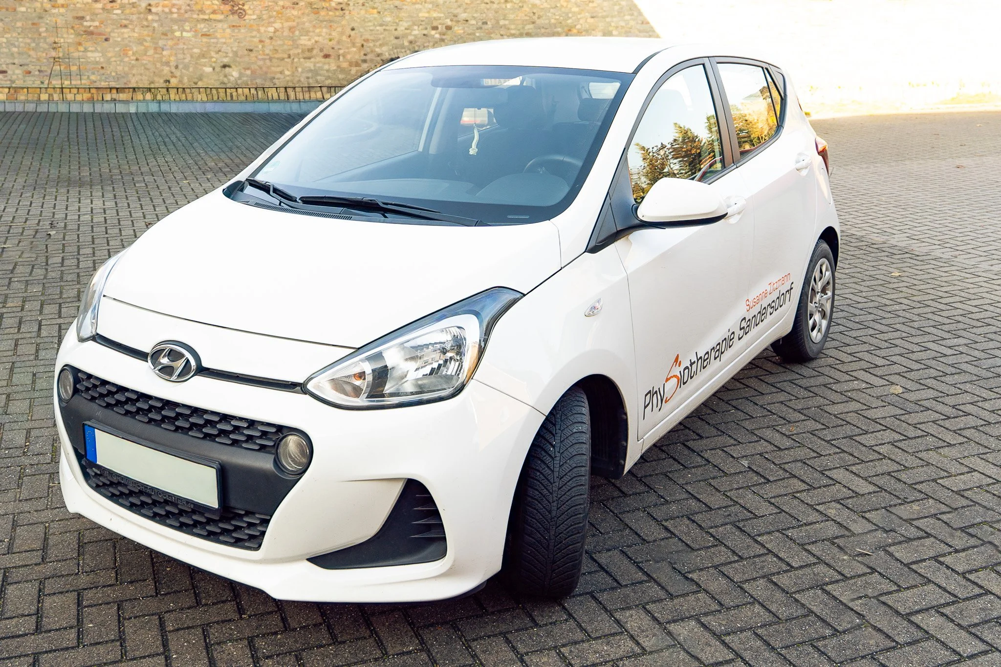 White Hyundai car parked on a brick pavement with therapy clinic branding on the side.