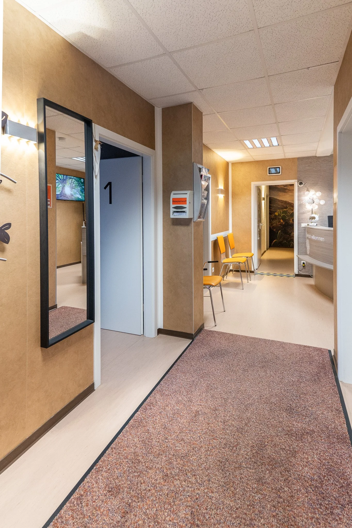 Hospital corridor with chairs, doors, a mirror, and reception desk.