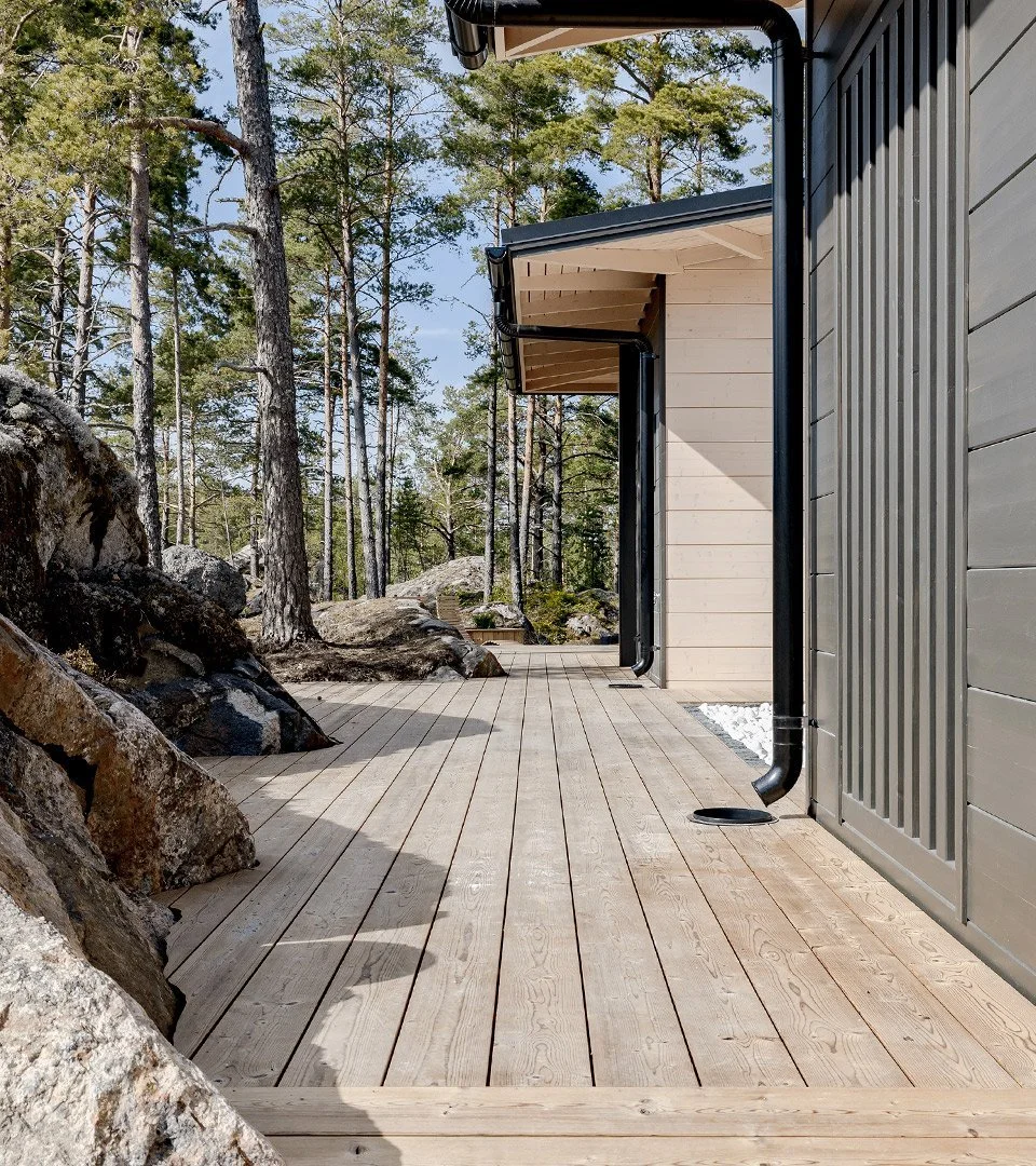 A modern house with a wooden deck surrounded by trees and rocks.