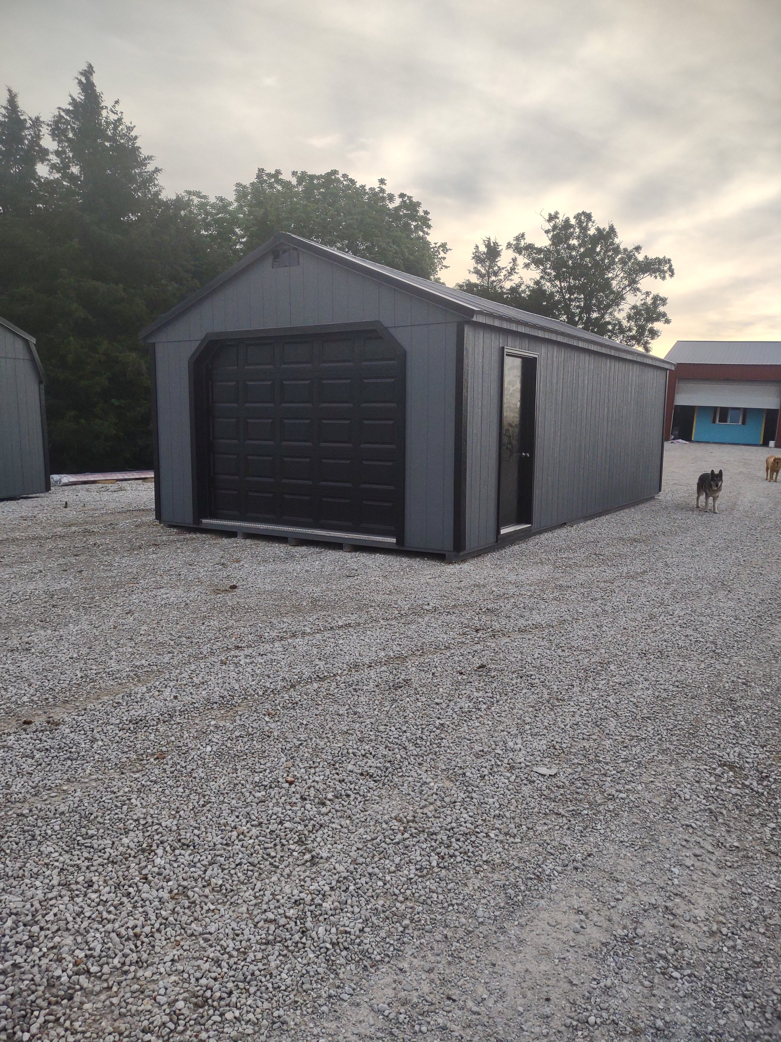 A small, gray metal shed with a black garage door and an insulated side door. For sale by Premium Structures LLC in Fair Play, Missouri.