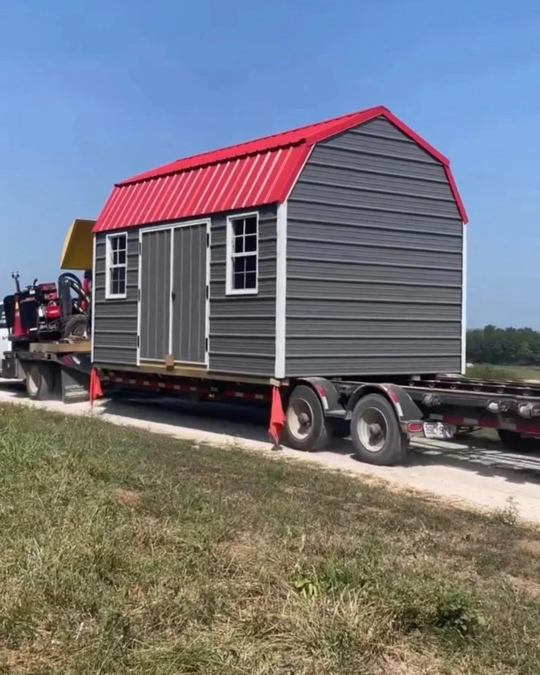 A small gray shed with a red metal roof on a flatbed trailer. Lofted Utility Shed in Fair Play, Missouri. Built by Premium Structures LLC.