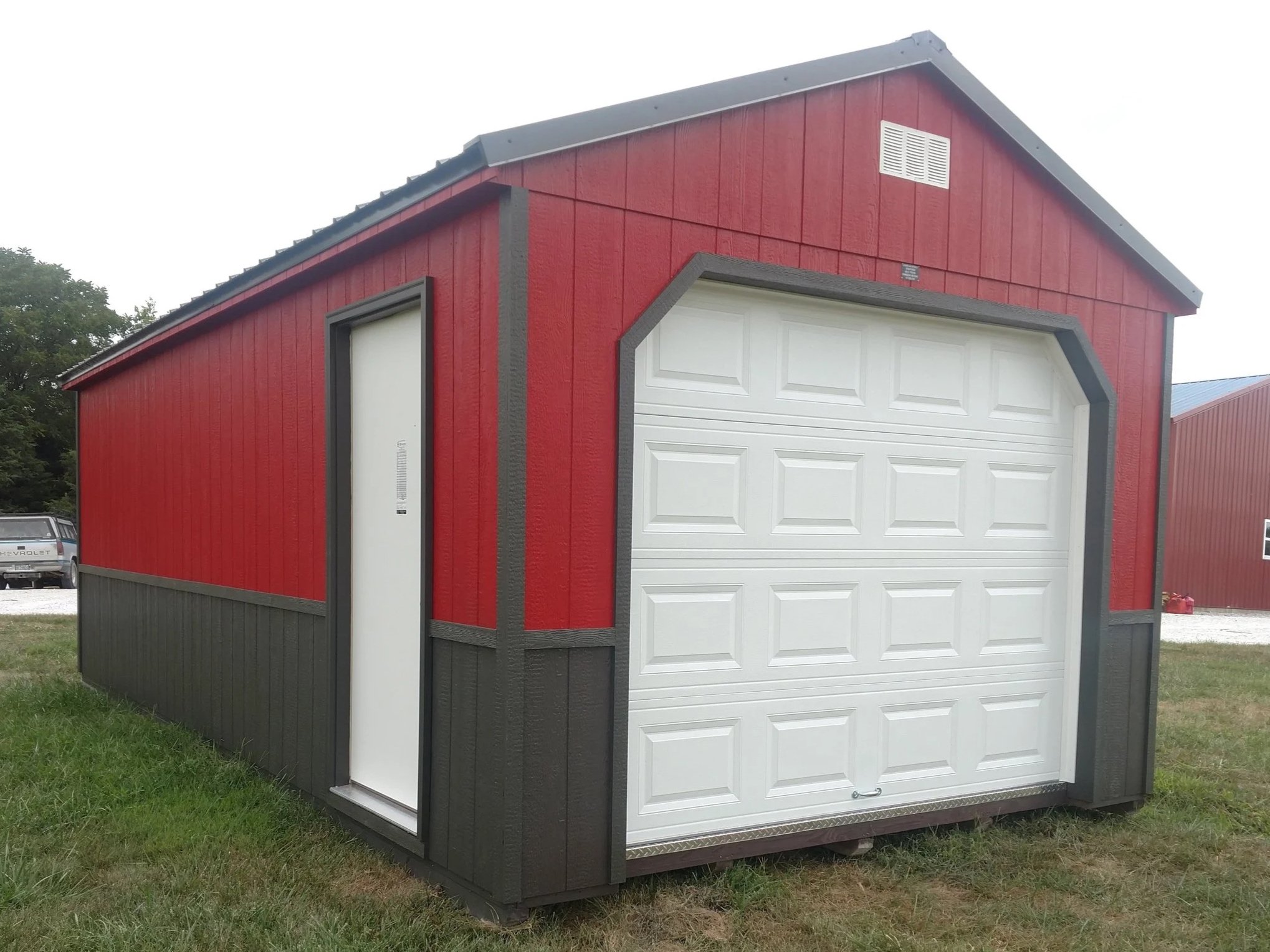 A red and white garage-style shed with black trim in a grassy area.