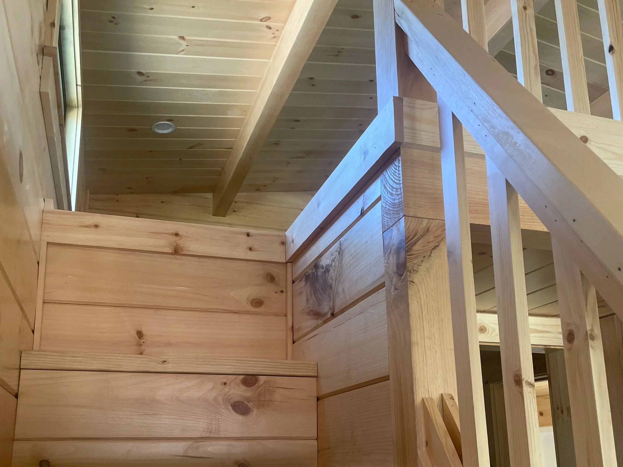 Interior view of a wooden staircase under construction, showing unfinished wood steps, railings, and wall paneling.