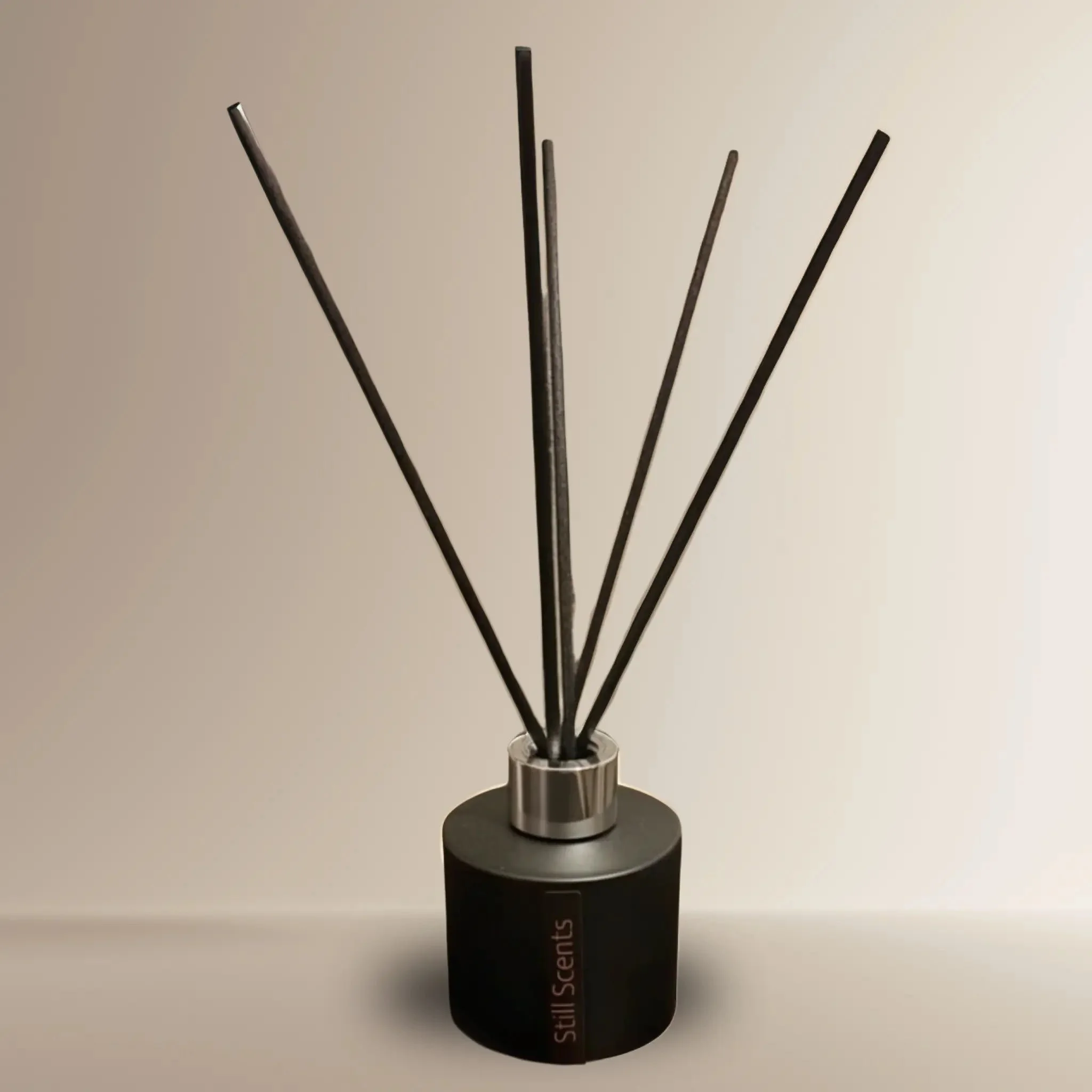 A black essential oil diffuser with black reed sticks on a white surface against a plain wall.