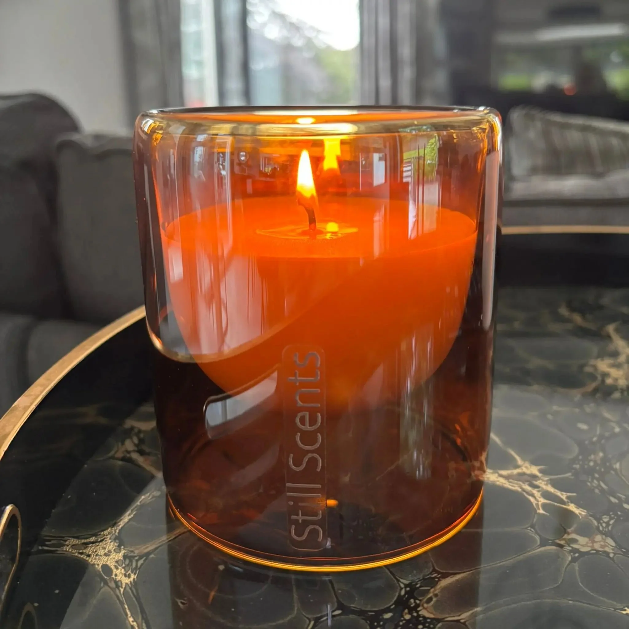 A lit candle inside an orange glass holder placed on a black marble surface.