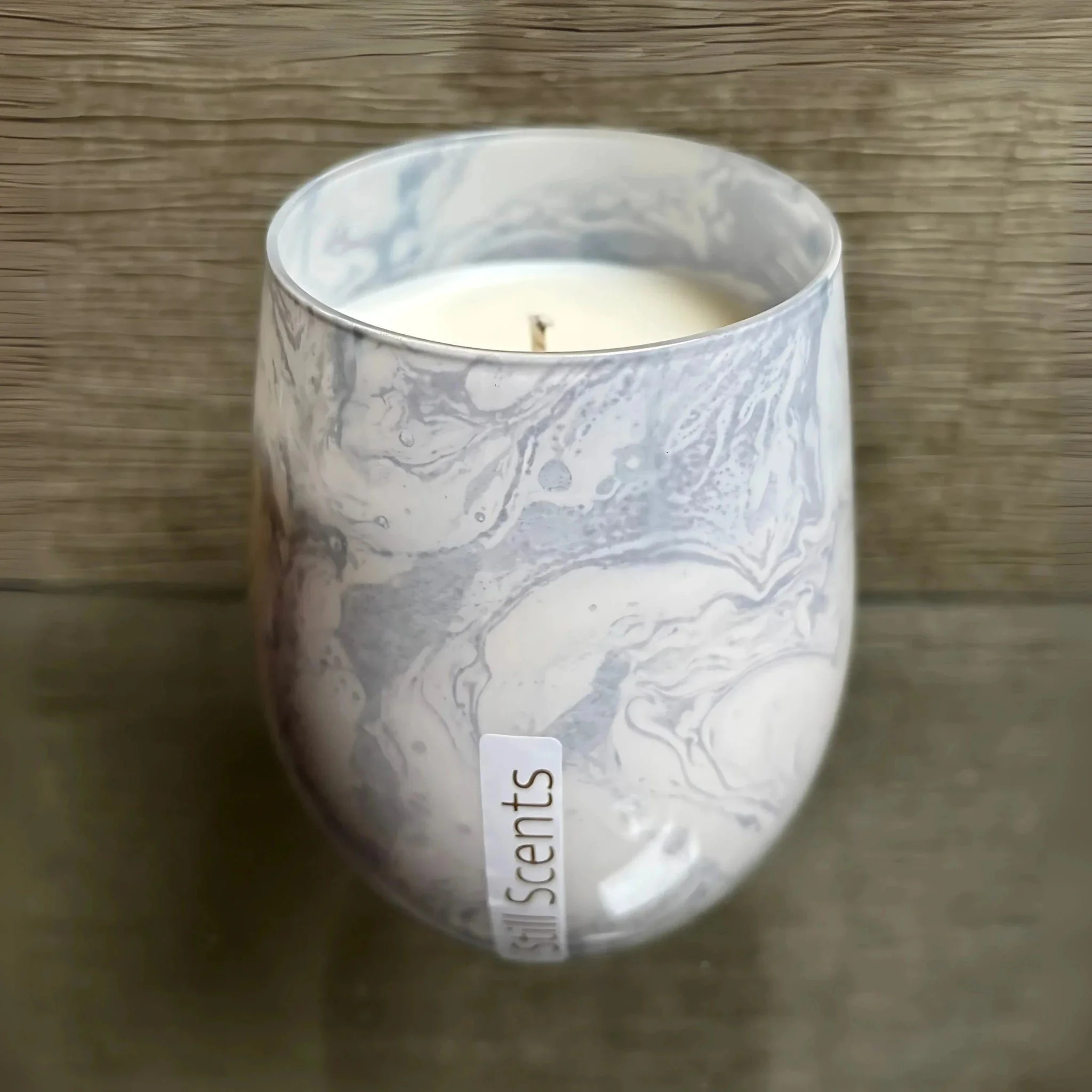 Decorative scented candle in a marbled glass holder labeled 'Scent' with a wooden background.