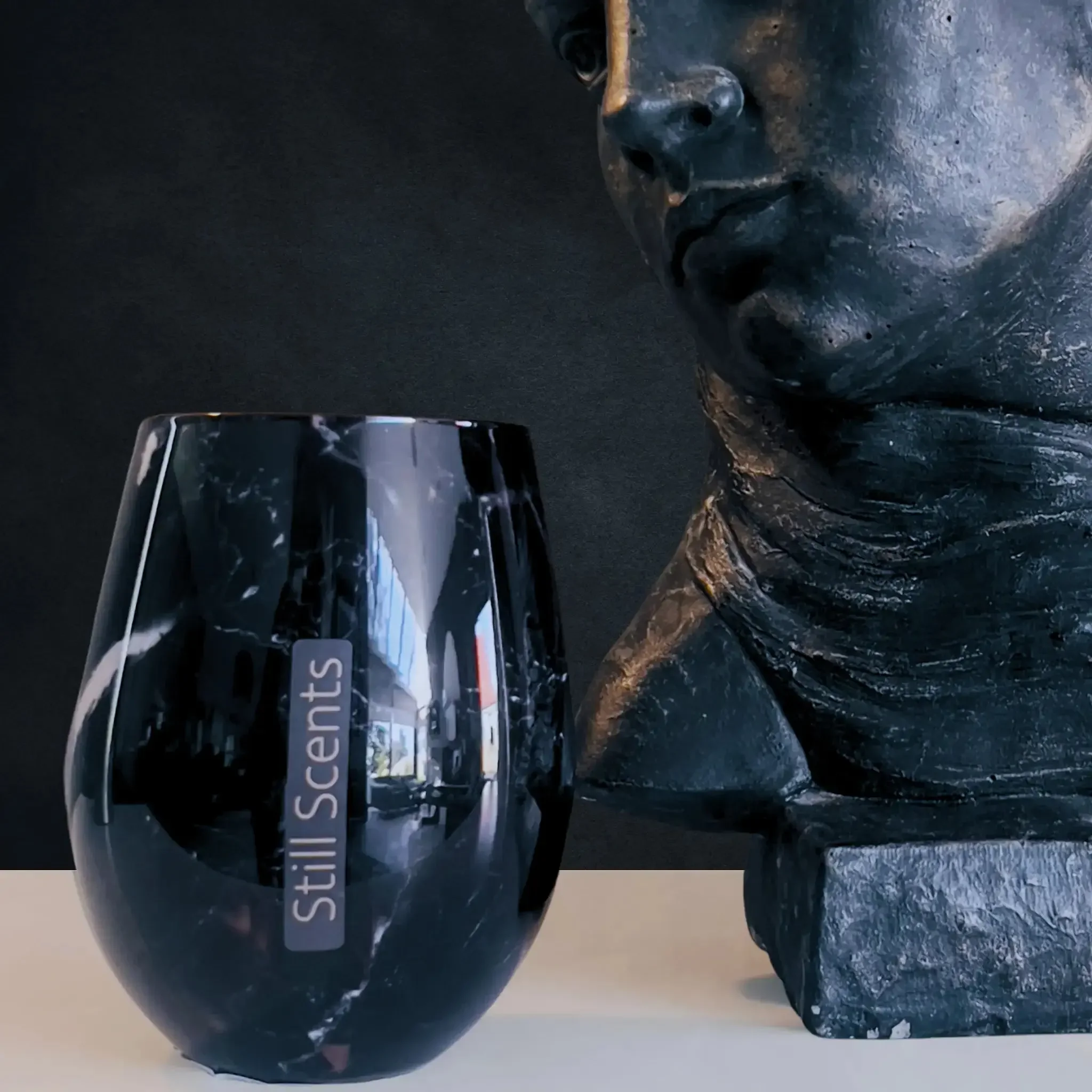 Black marble candle beside a black stone bust. Dark Background.
