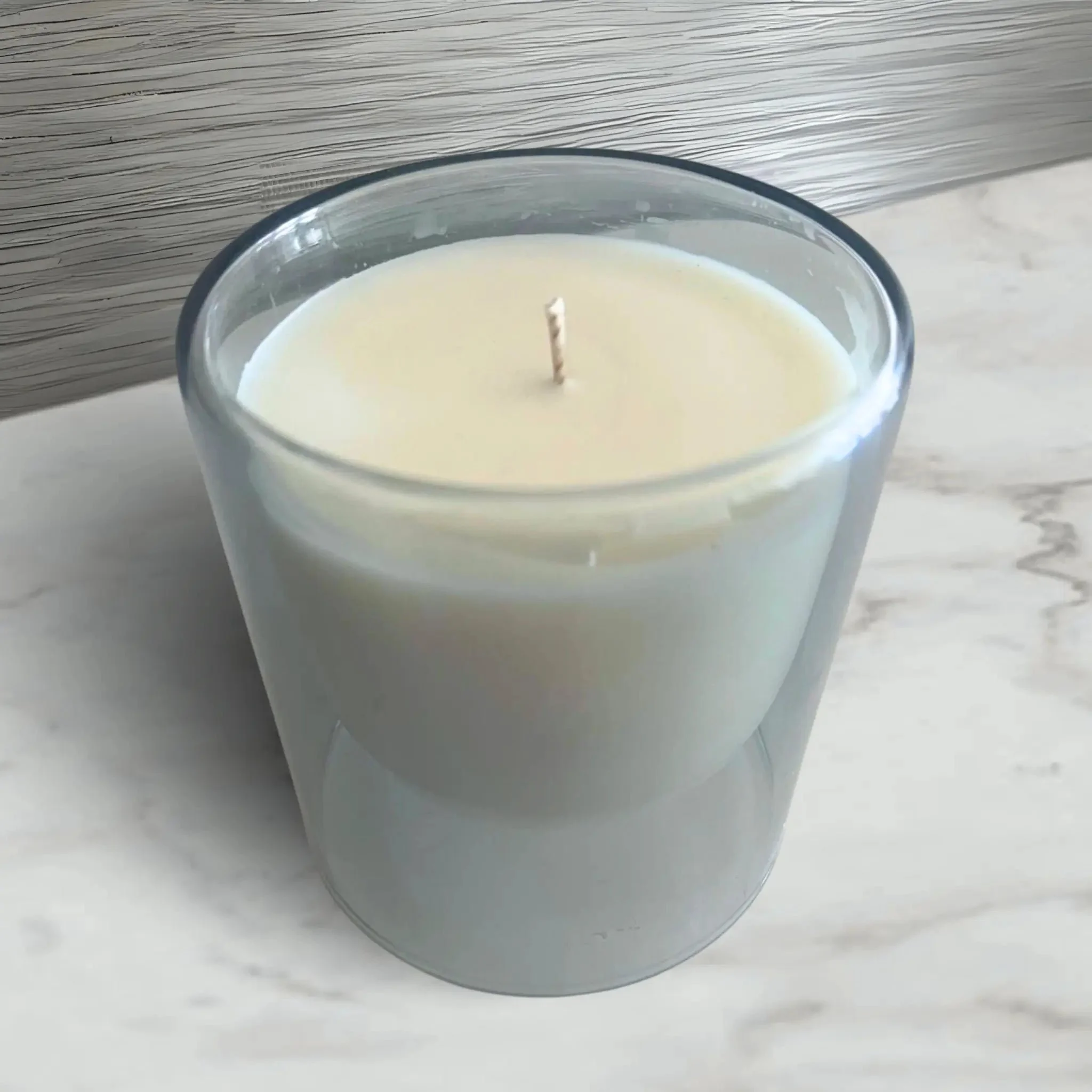 A white candle in a grey glass holder on a marble surface.