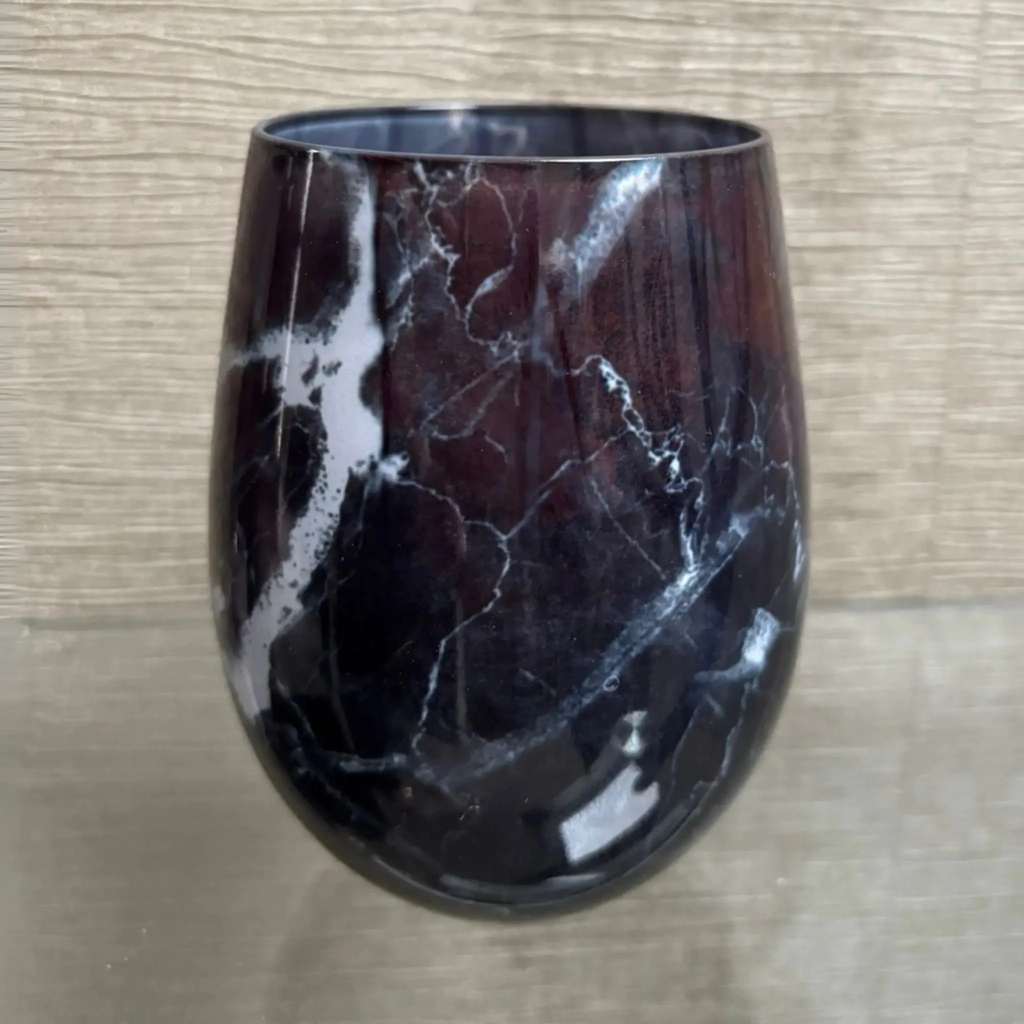 A black marbled glass candle placed against a light beige textured background.