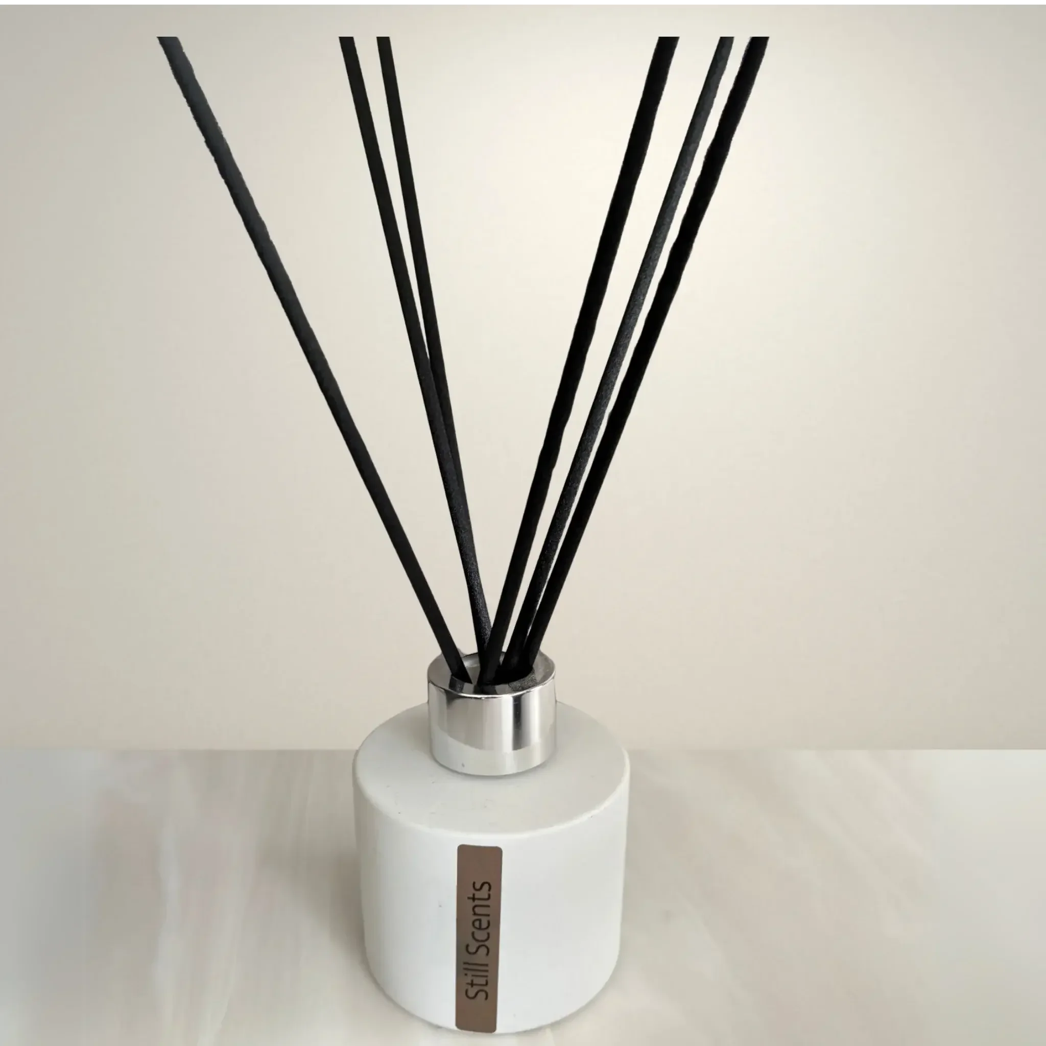 A white diffuser bottle labeled "Still Scents" with black reed sticks extending from the top.