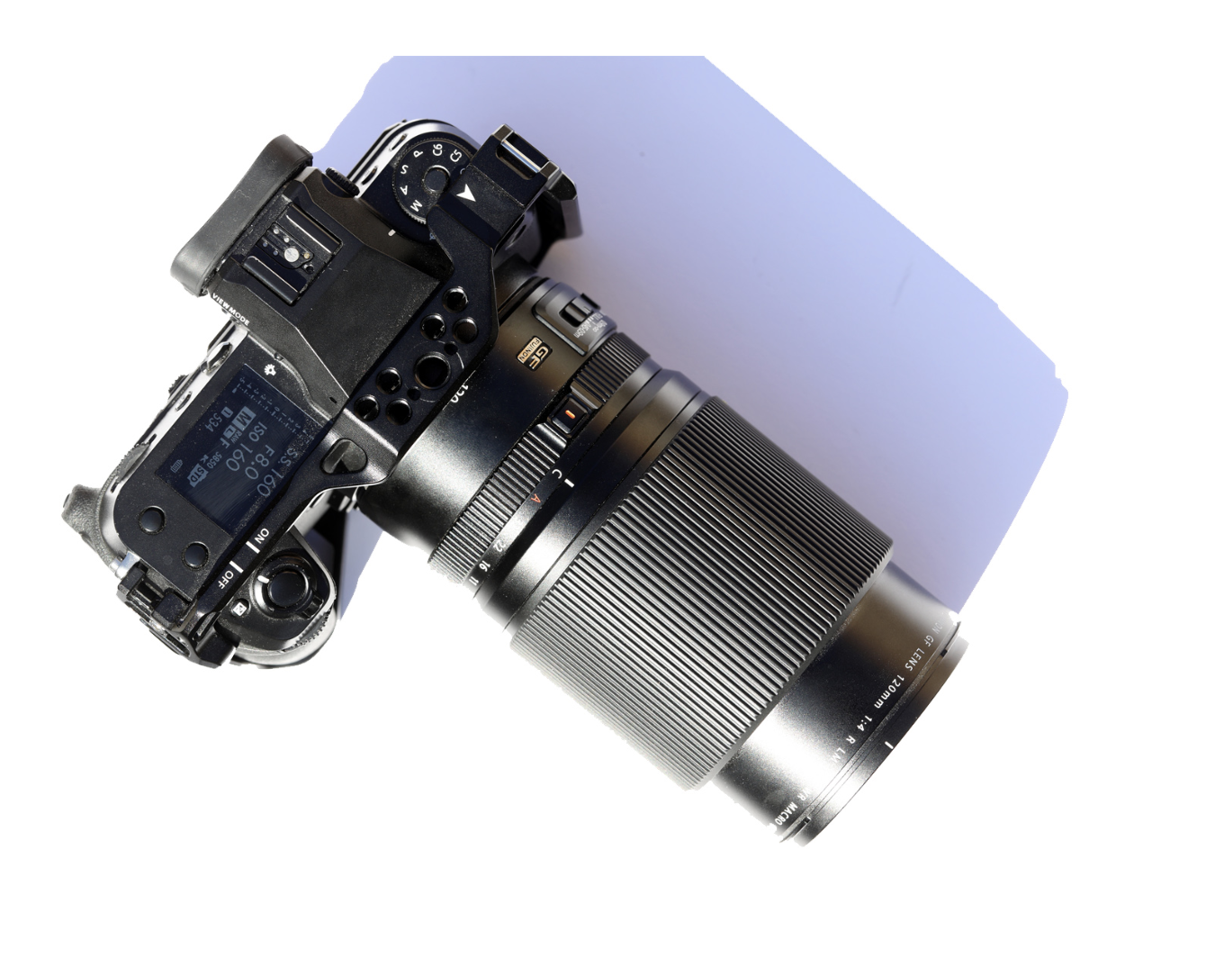 A digital mirrorless camera with a large zoom lens attached, placed on a white surface.