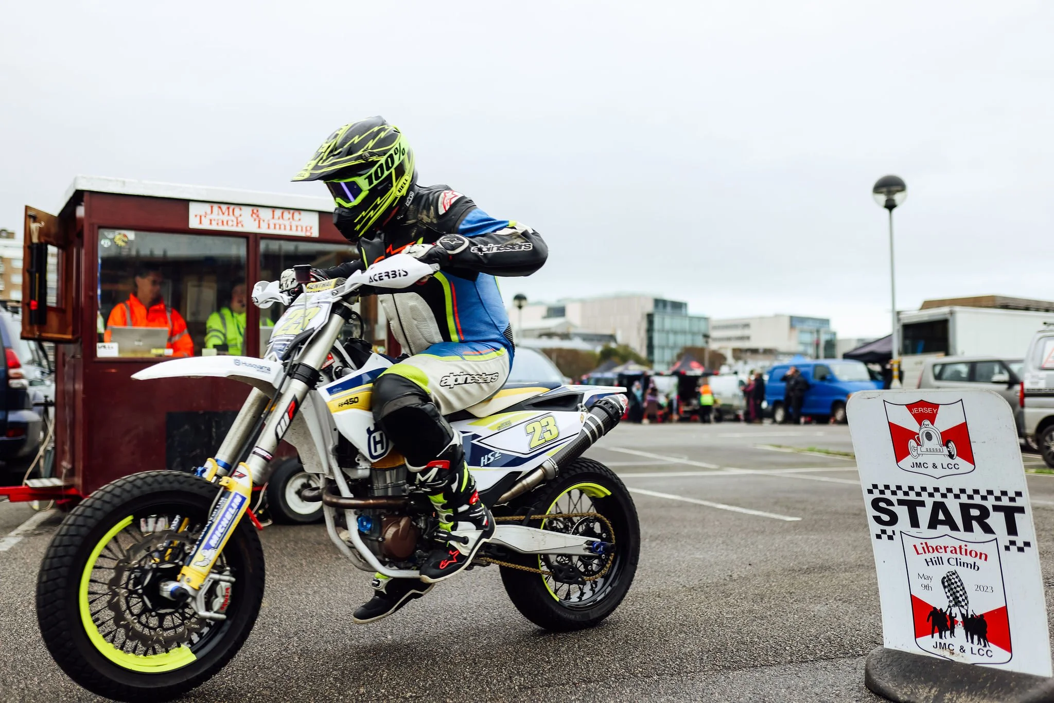 Motocross rider on a white and blue dirt bike at the start line of a hill climb race, with a sign reading "START Liberation Hill Climb May 9th, 2023" in the foreground.