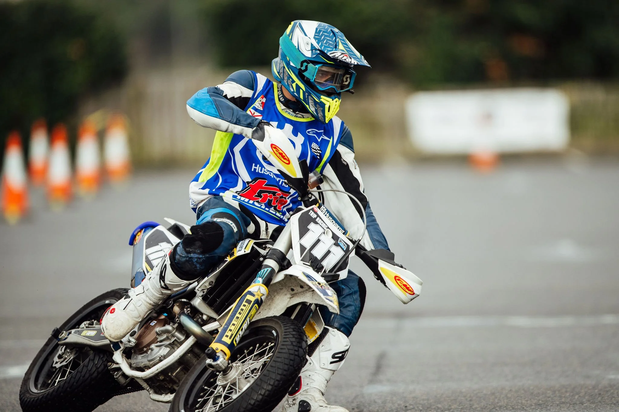 A motocross rider in a blue, white, and black racing suit riding a dirt bike on an outdoor track.