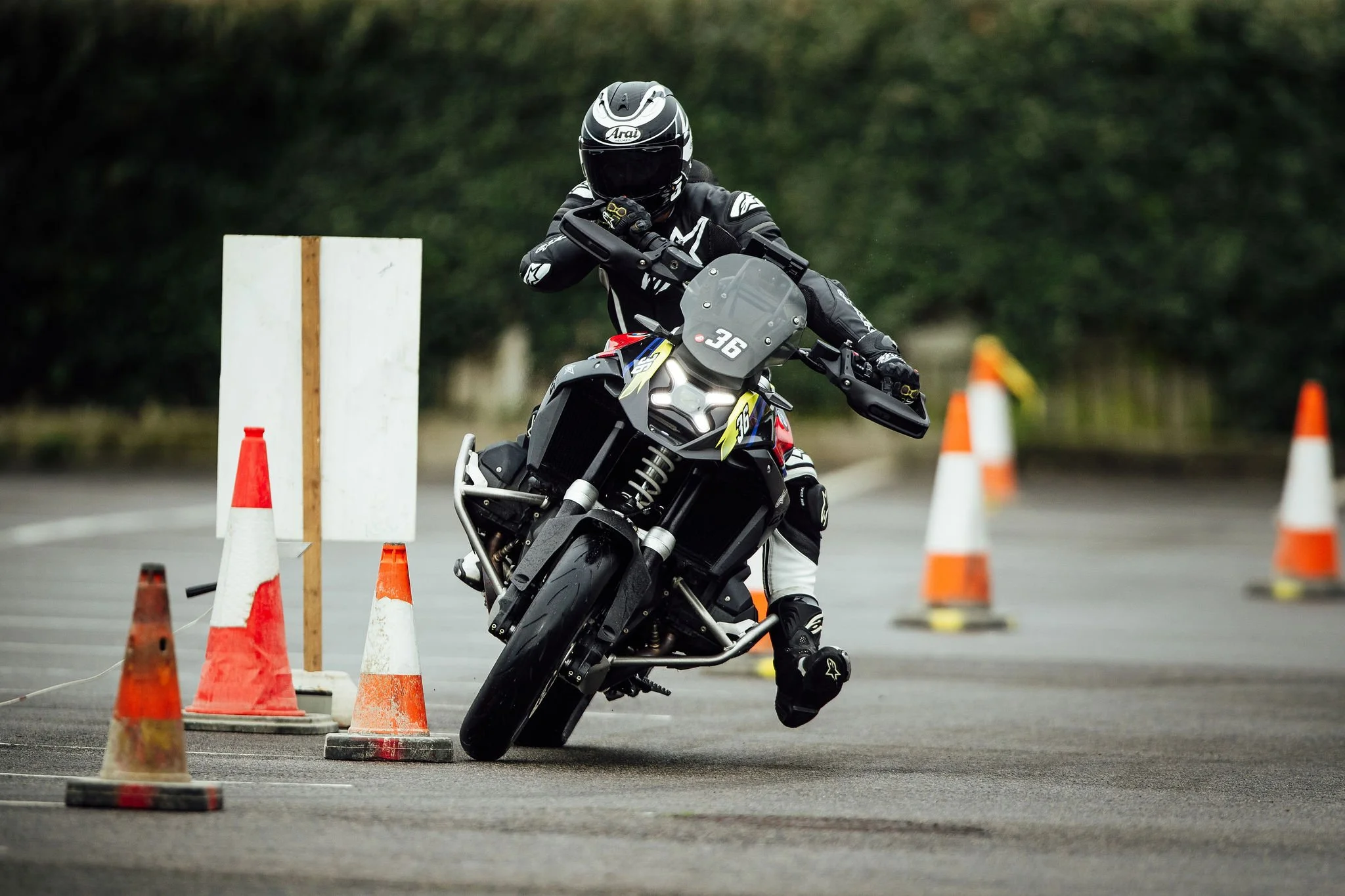 Motorcycle rider navigating through orange traffic cones on a paved course with greenery in the background.