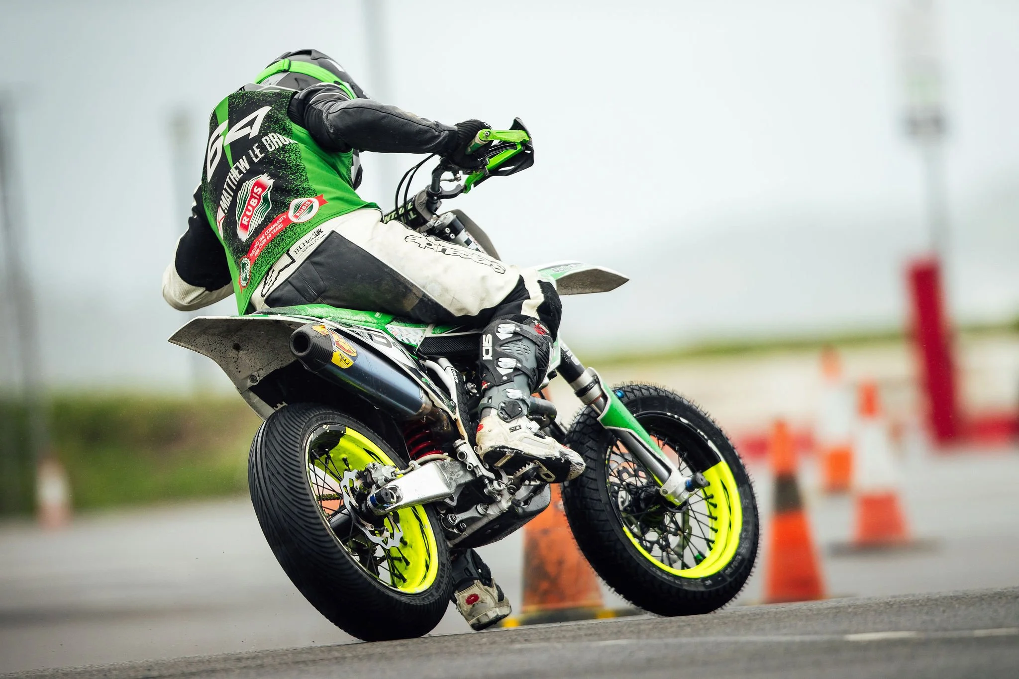 A motocross rider leaning into a turn on a dirt track, wearing green and white gear, riding a green motorcycle with neon yellow wheels.