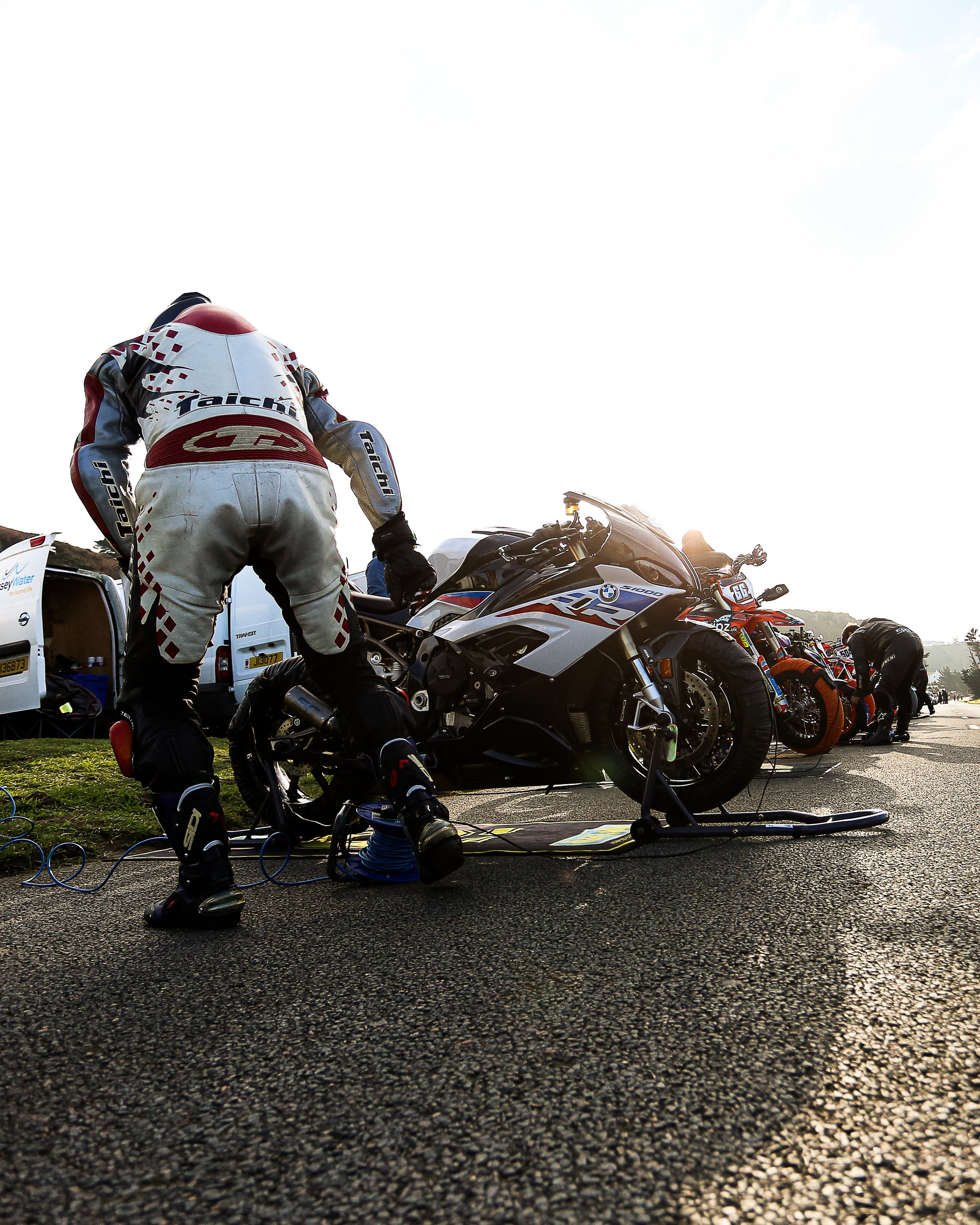 Motorcycle racers during a pit stop, with one mechanic working on a BMW S 1000 RR motorcycle on a racetrack.