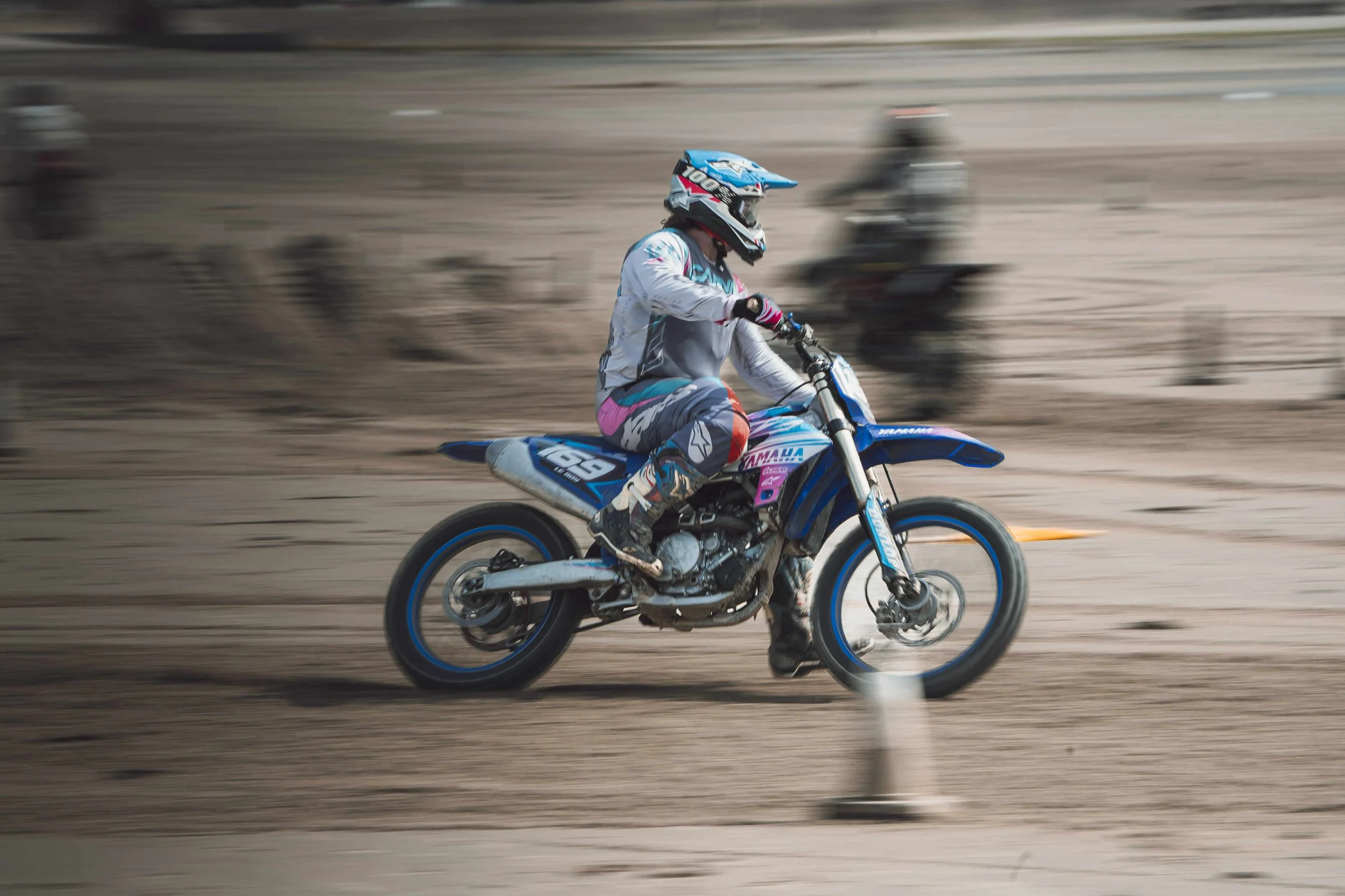 Motocross rider in gear riding a dirt bike on a sandy track with motion blur