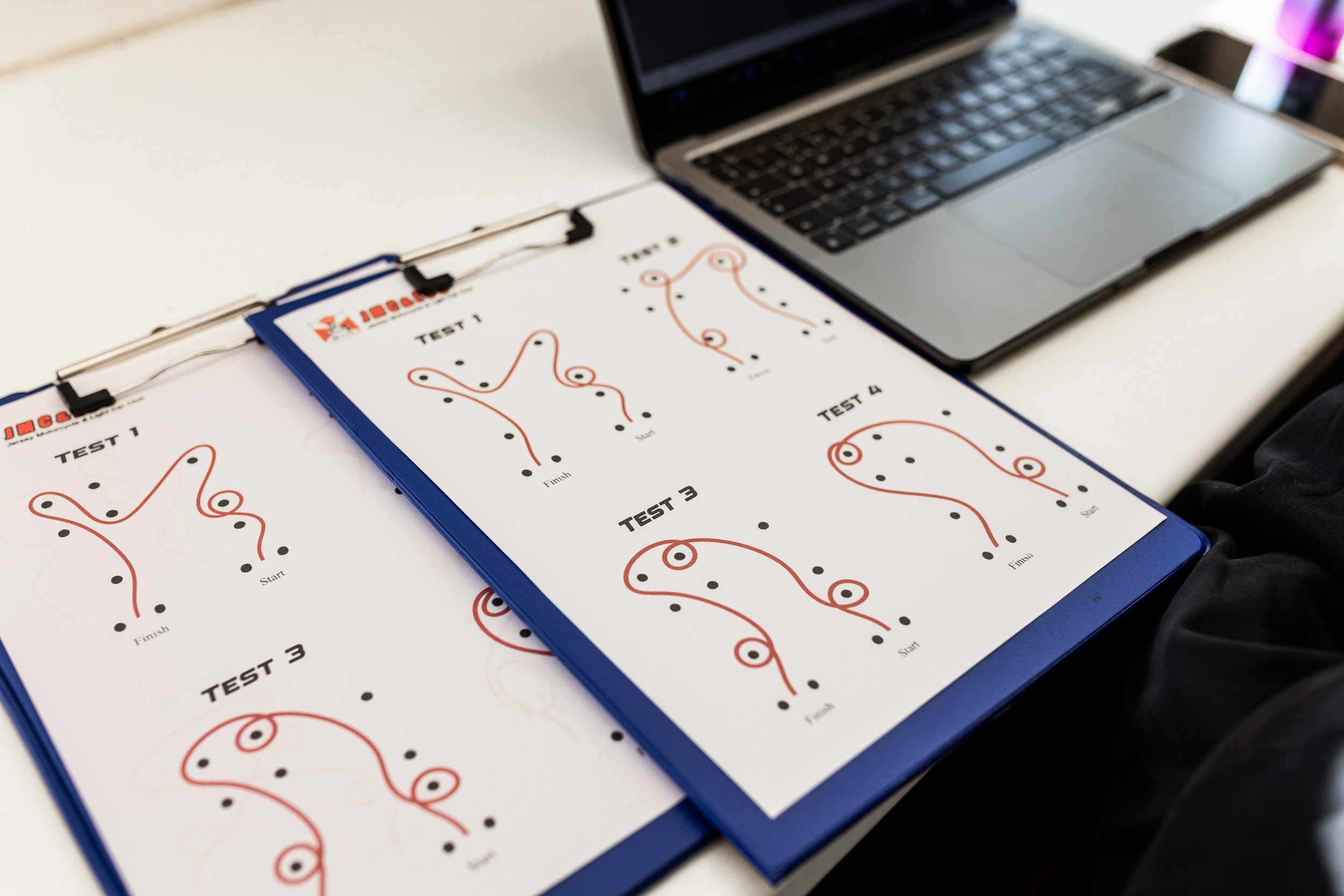 Printed testing sheets with multiple patterns of connected dots and lines on a desk, with a laptop nearby.