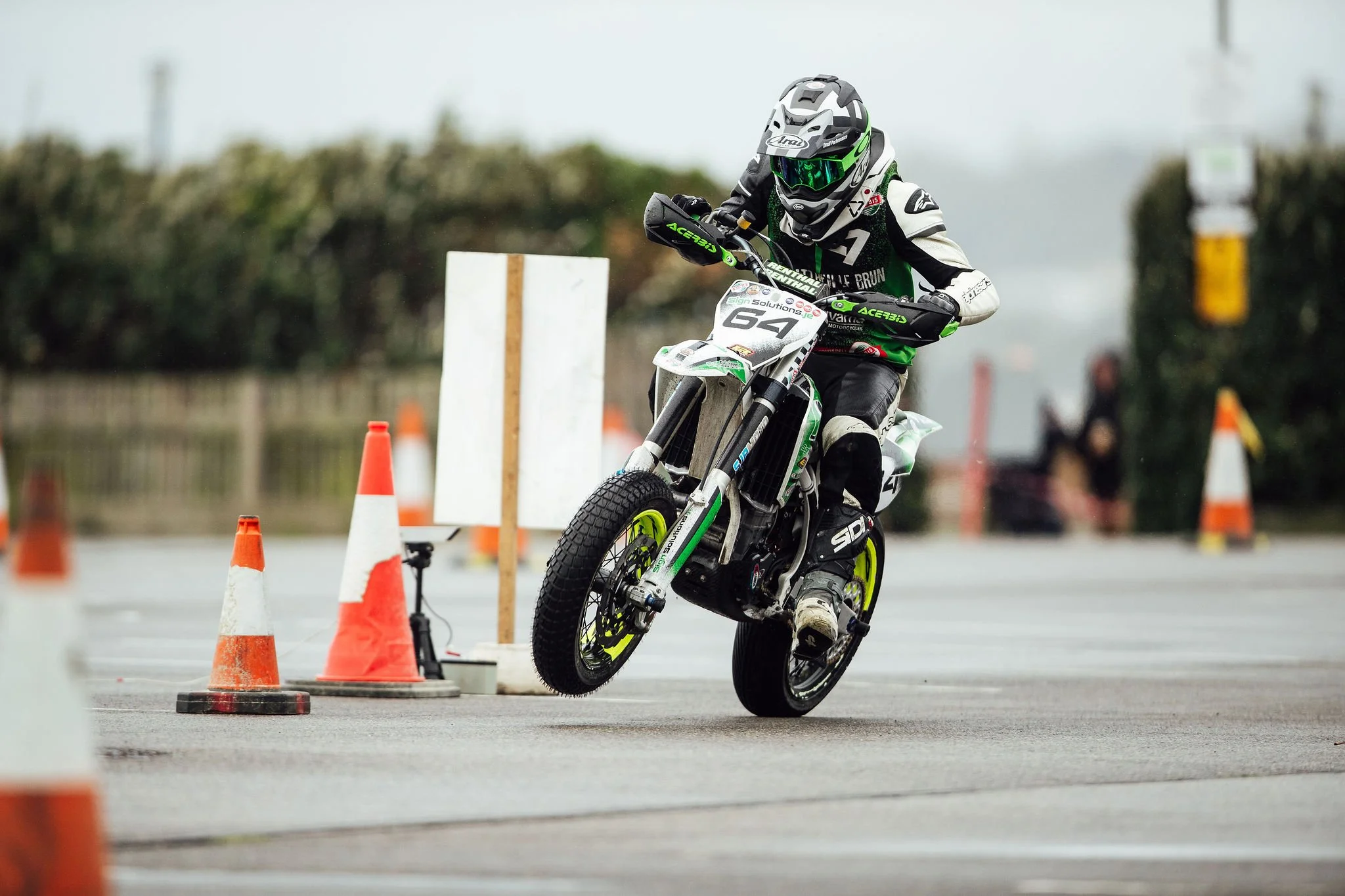 A motorcycle rider in gear and helmet leaning into a turn around orange cones on a paved course.