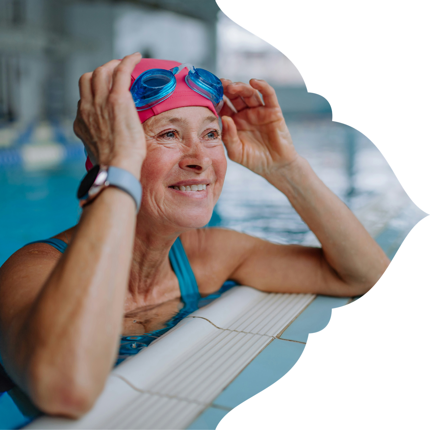 An older woman with a pink swim cap and blue goggles smiling at the edge of a swimming pool.