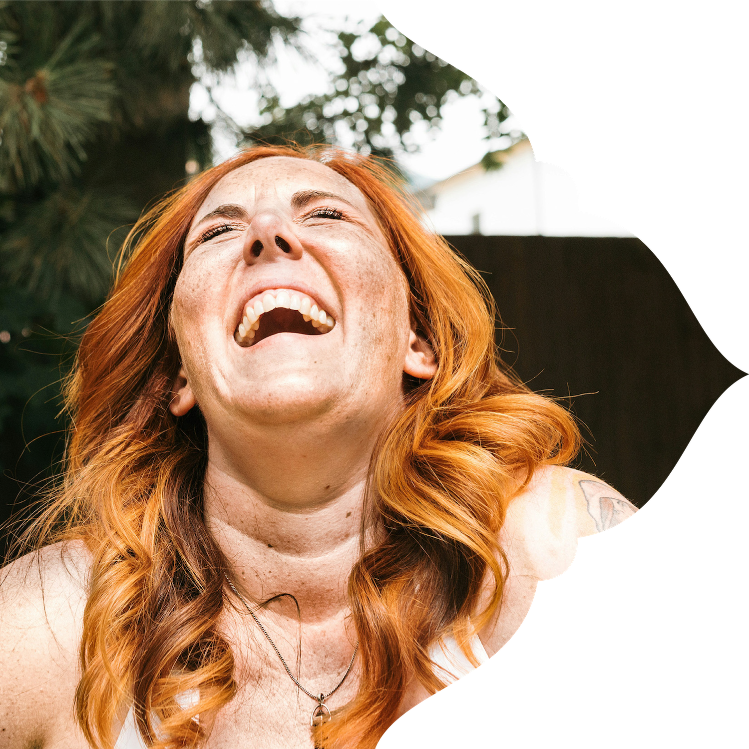 A woman with red hair laughing outdoors.