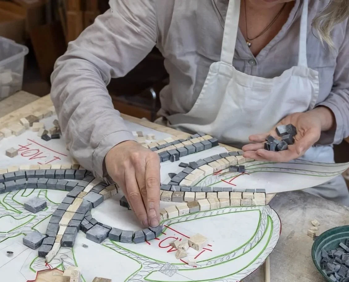 Person working on a mosaic design, placing small tiles on a drawn pattern on paper.