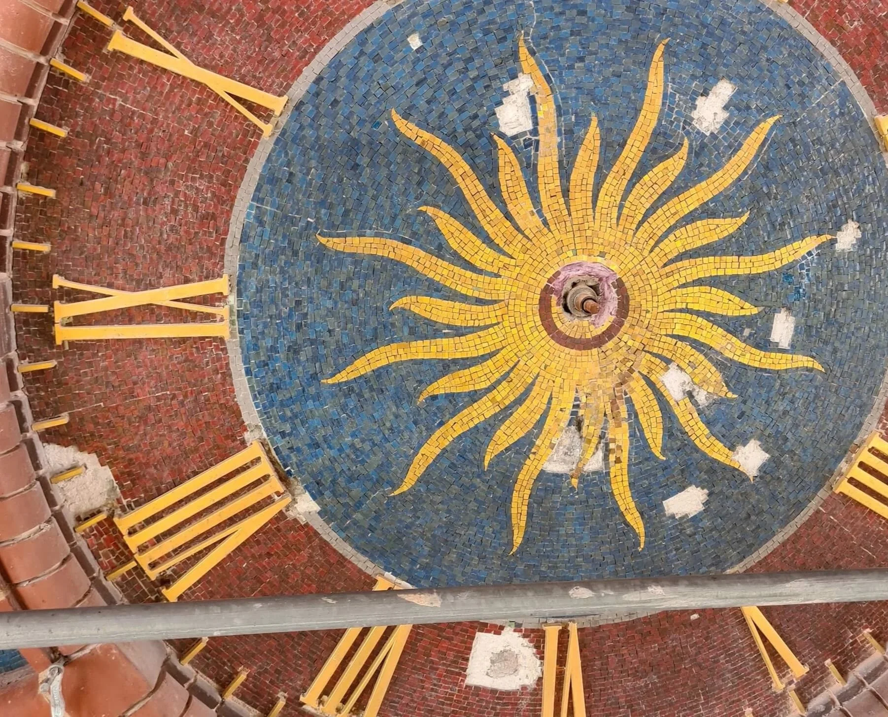 A decorative mosaic of a yellow sun with rays on a blue circular background, with surrounding red brick and yellow benches.
