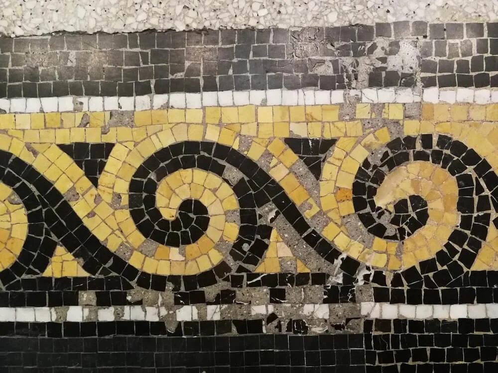 Close-up image of a mosaic floor with yellow and black tiles forming a swirling pattern.