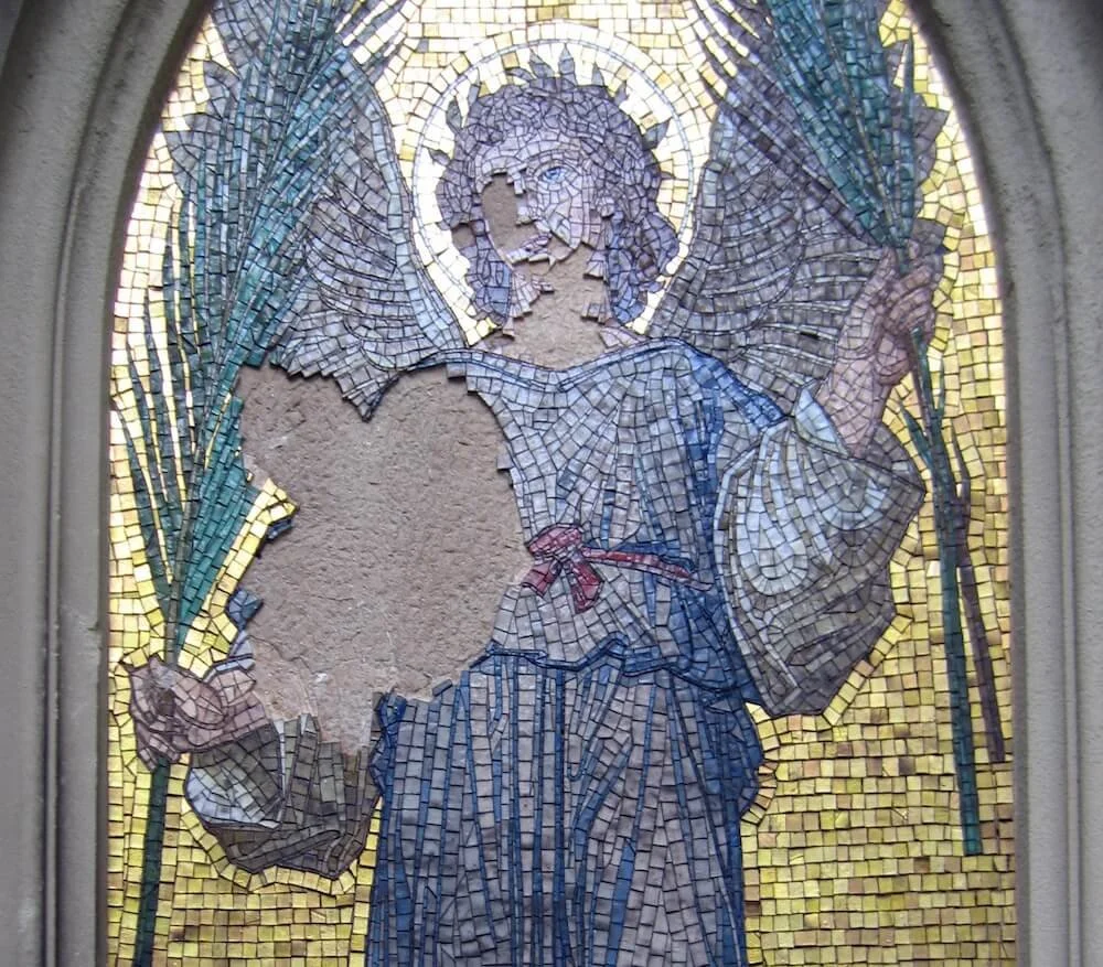 Mosaic art of an angel with wings, holding a spear, with a halo around its head, and a missing section in the chest area.