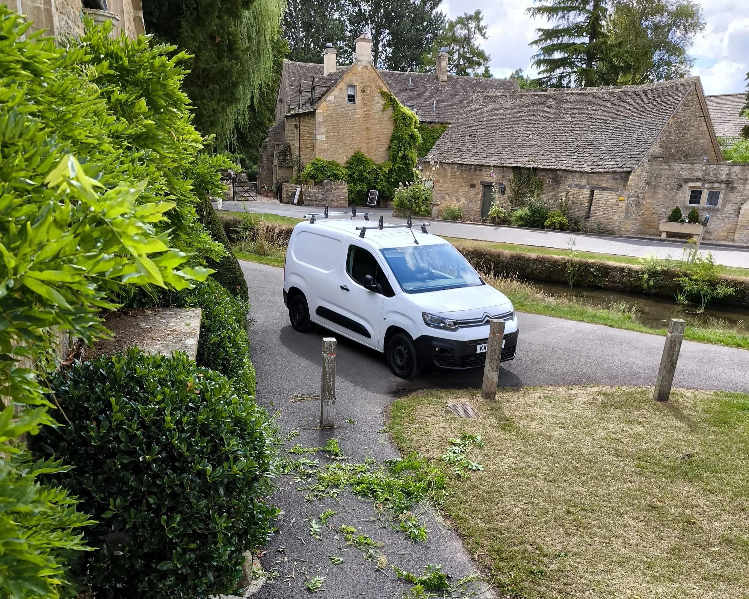 White work van surrounded by freshly cut grass in front of a rustic cottage.