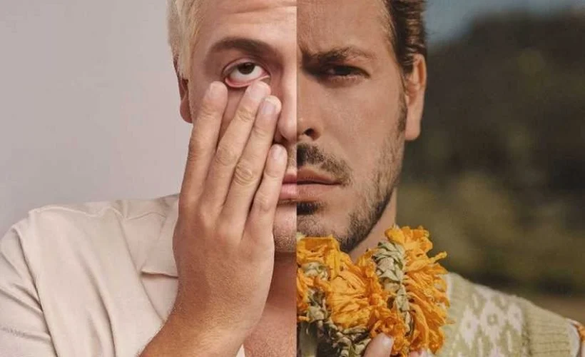 A split image of a man with changed appearance. One half shows a man with blonde hair and a white shirt, covering one eye with his hand. The other half shows the same man with darker hair, a beard, wearing a yellow and green floral shirt, and holding a marigold flower.