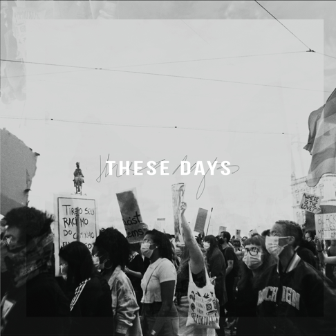 A group of people protesting, holding signs and wearing masks in an outdoor setting.