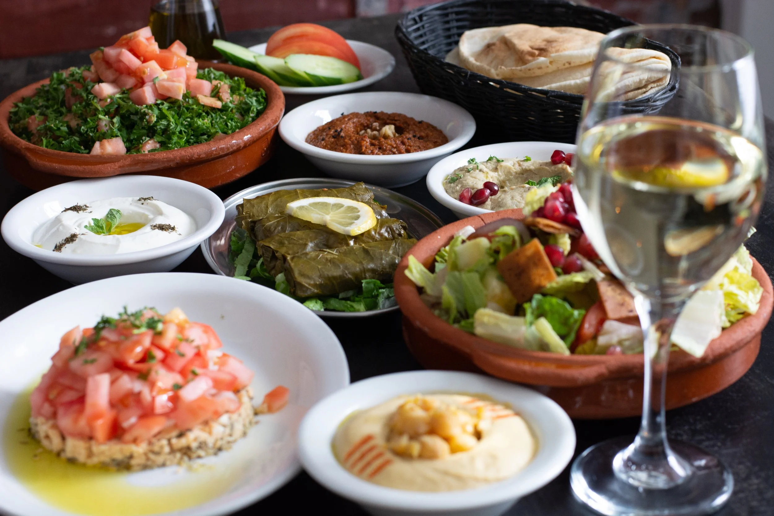 Assortiment de plats méditerranéens avec salades, houmous, pain, et un verre de vin blanc.