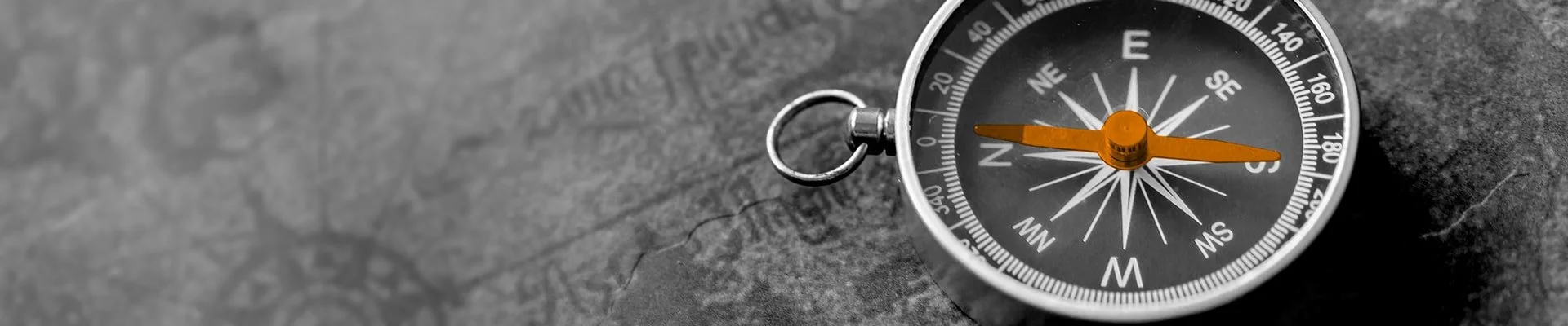 A close-up of a compass on a gray textured surface, showing cardinal directions and needle pointing northwest.